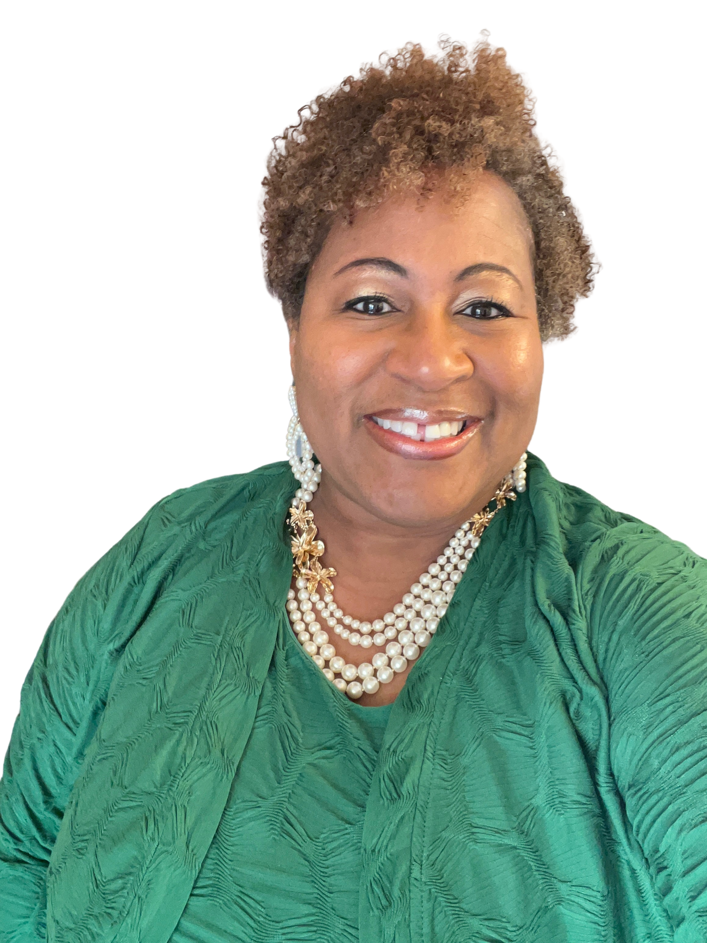 A smiling woman with short curly hair, wearing a green textured dress, pearl necklace, and pearl earrings, posed against a plain white background.
