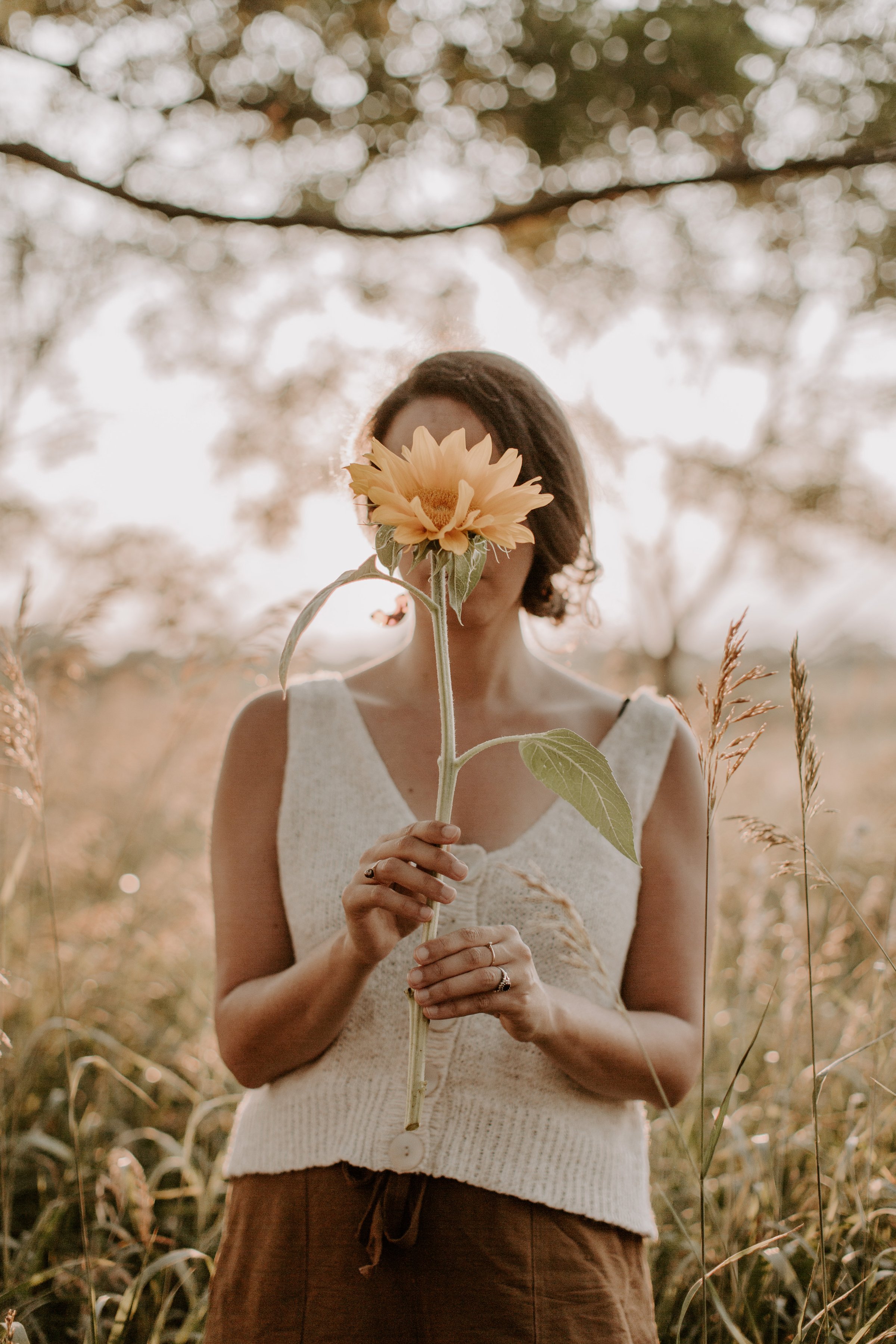 Woman holding a sunflower in front of her face outdoors during sunset
