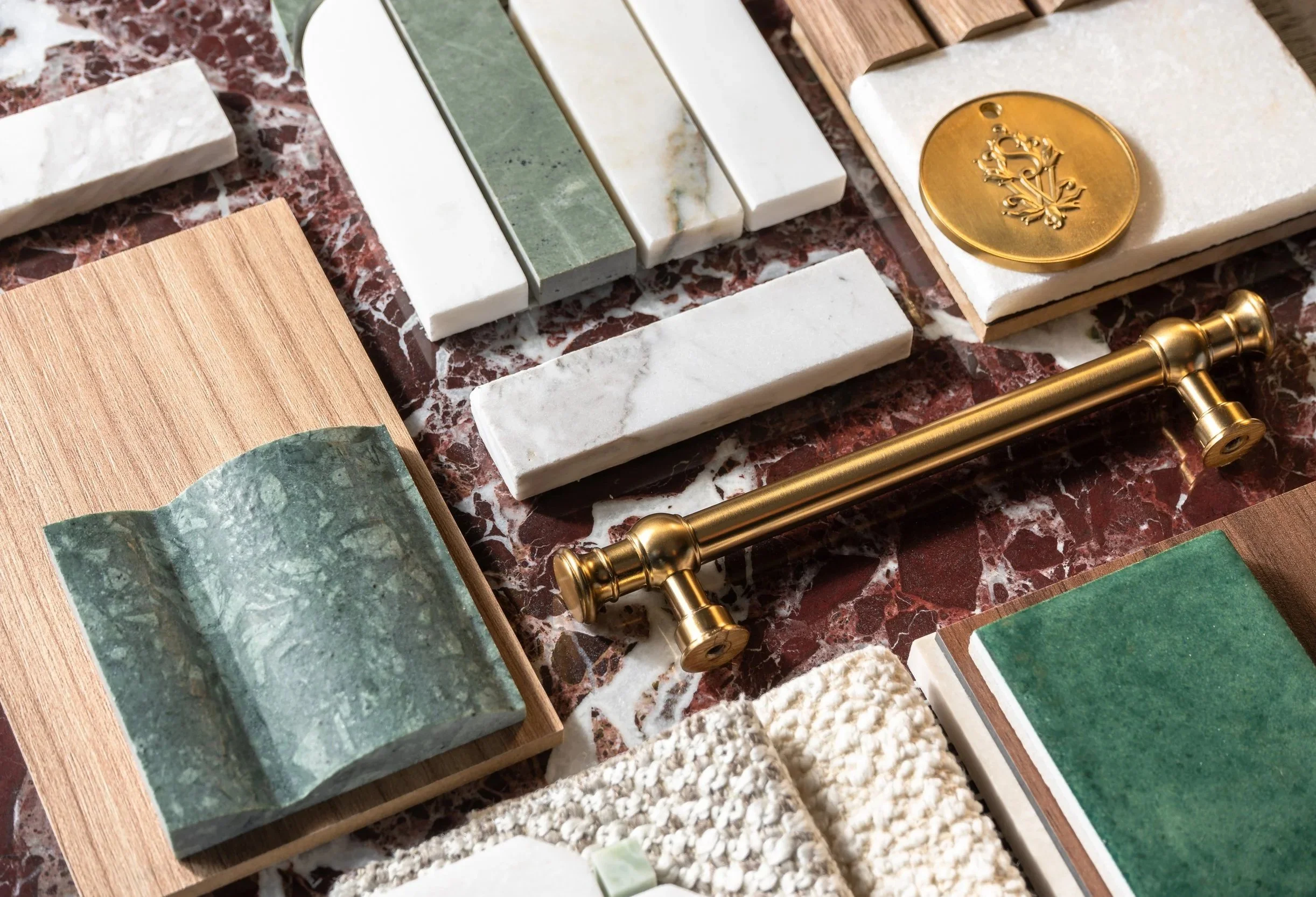 Samples of white and green marble tile and mosaics, custom fabrics, wood flooring and brass bathroom cabinet hardware on a large red marble tile.