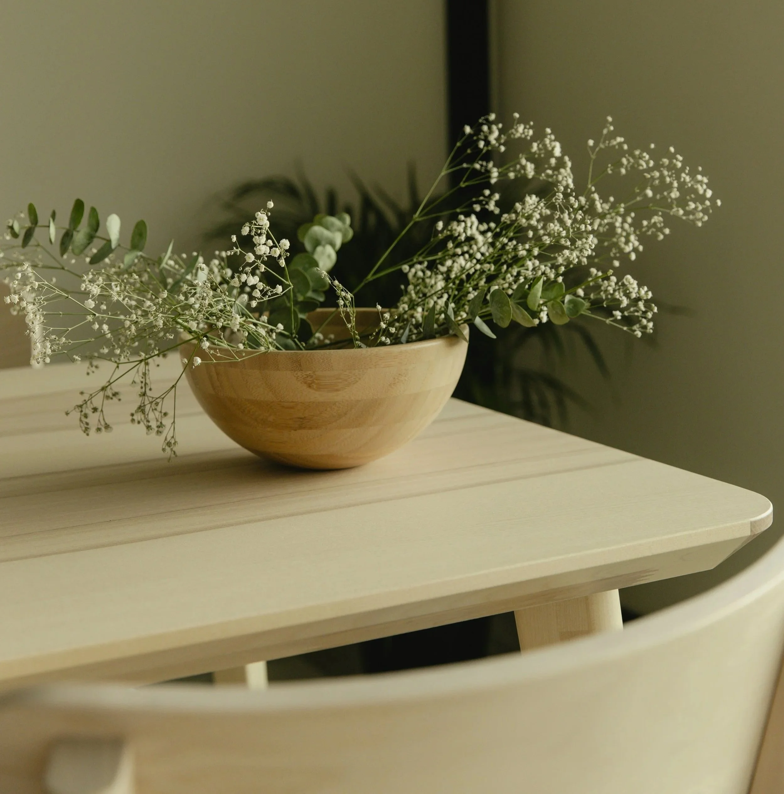 Baby's breath and greenery in a wooden bowl on a wooden minimalist natural neutral table.