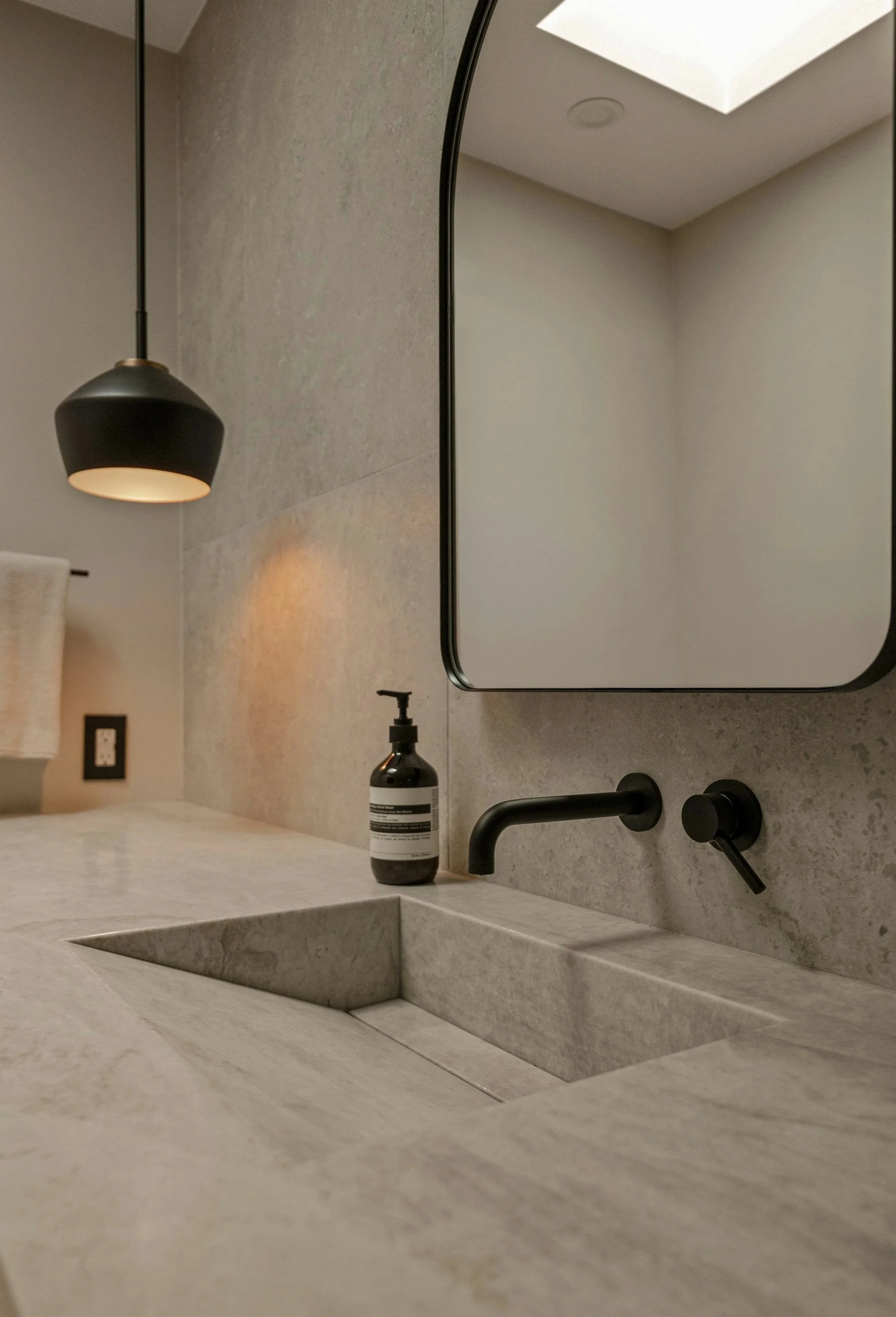 Bathroom vanity made of grey natural stone in a grey minimalist, modern interior with a matte black faucet and mirror on the wall