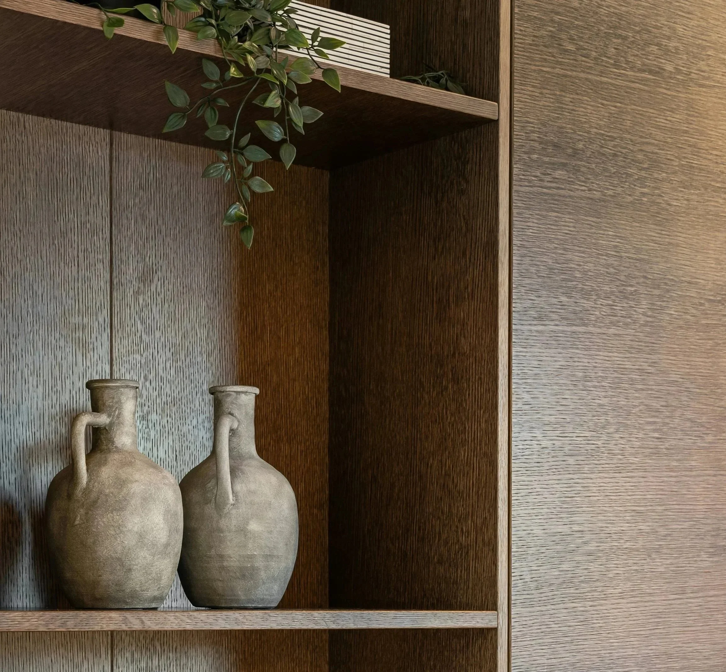 Beige ceramic vases and shelf decor with greenery on a sophisticated dark wood bookcase.