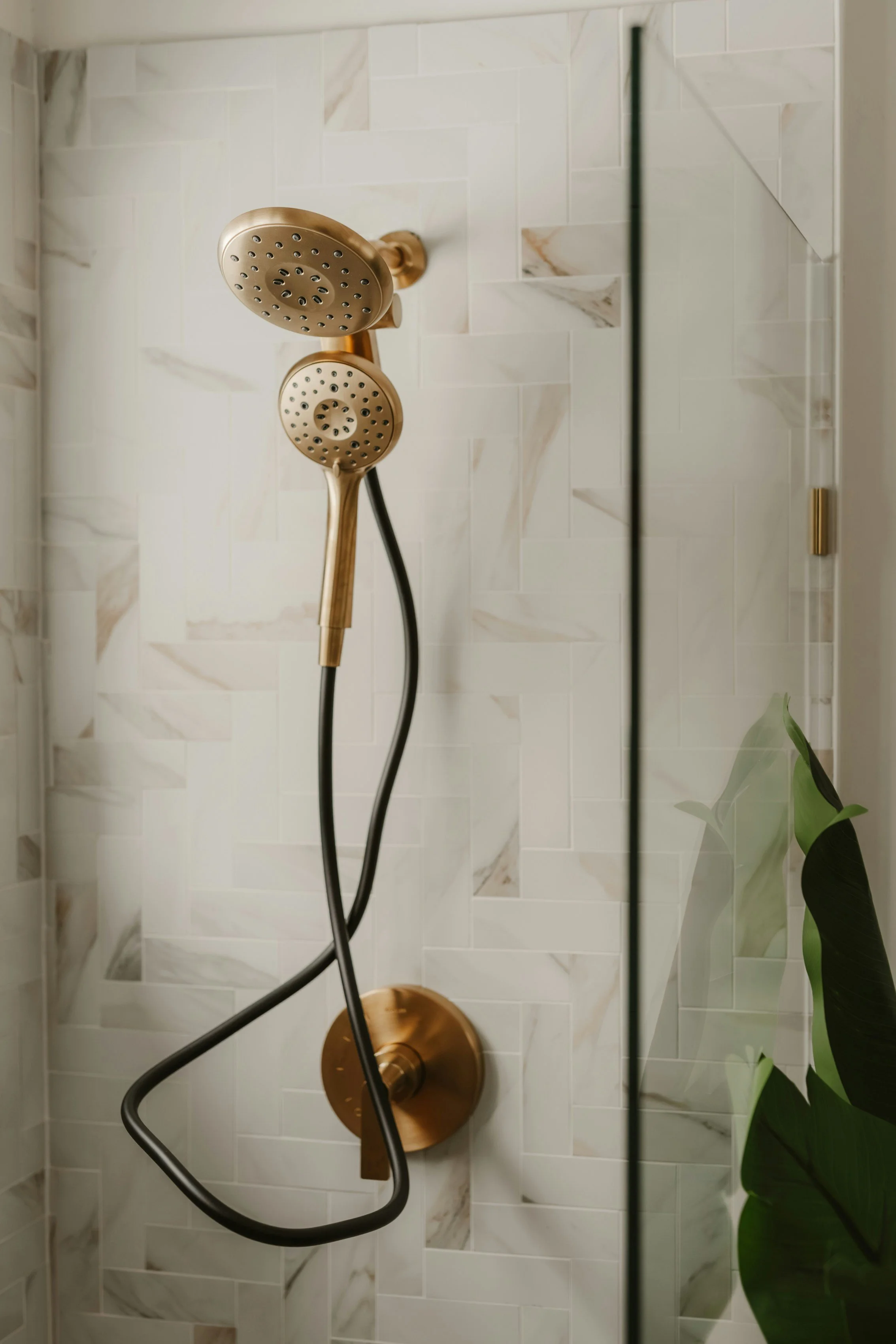 Modern, updated shower with white marble tile walls, dual bronze showerheads, and a glass shower door.