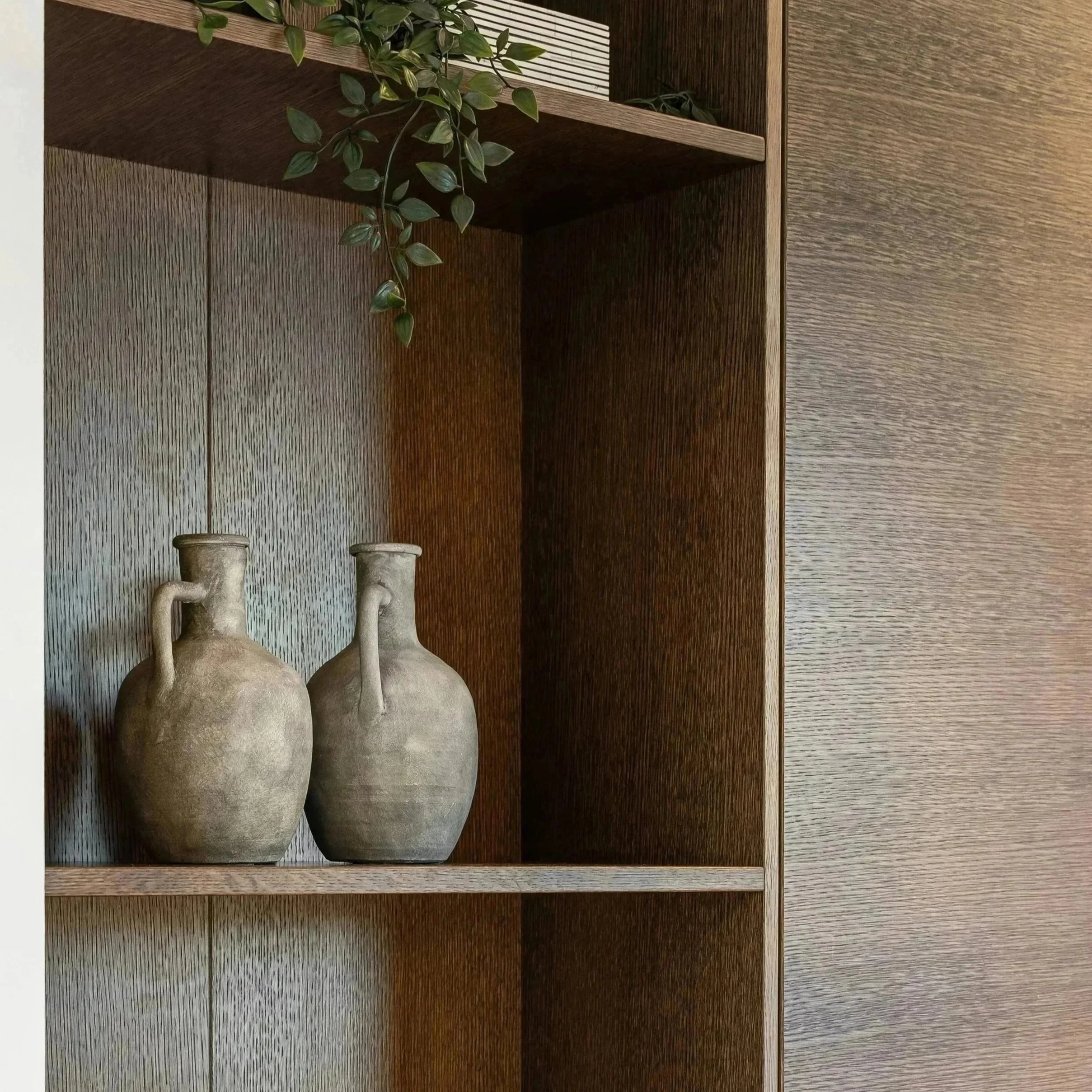 Beige ceramic vases and shelf decor with greenery on a sophisticated dark wood bookcase.