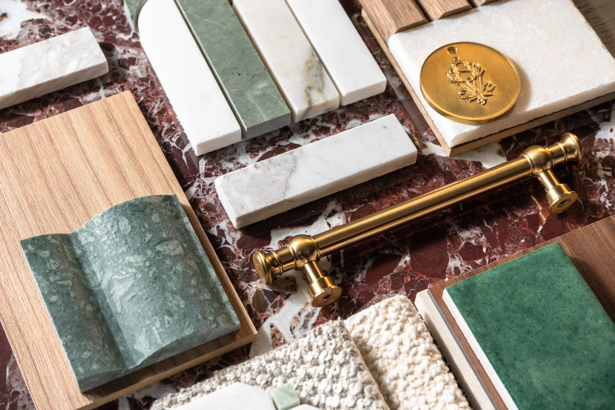 Samples of white and green marble tile and mosaics, custom fabrics, wood flooring and brass bathroom cabinet hardware on a large red marble tile.