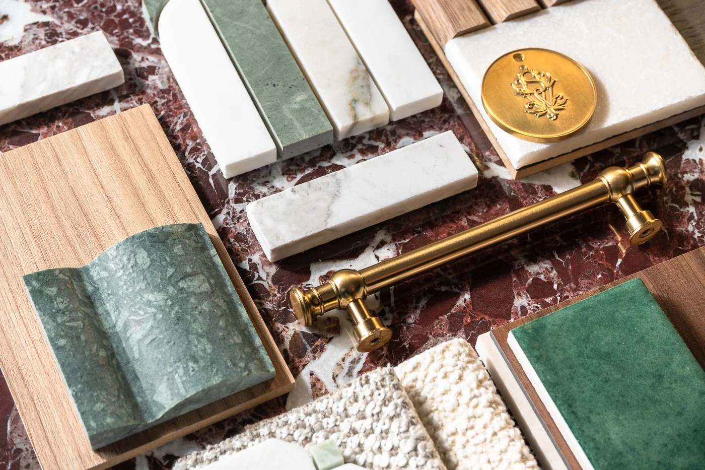 A variety of tile samples, including marble, stone, and ceramic tiles, arranged on a marble surface with a brass curtain rod and a decorative brass medallion.