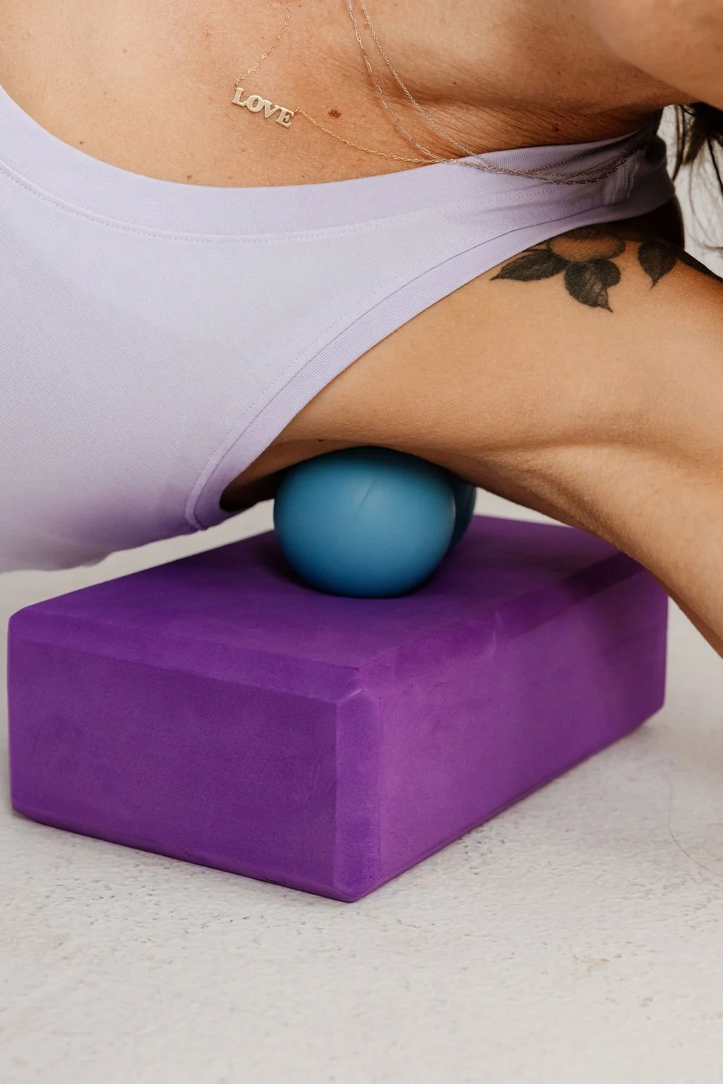 Close-up of Lexy Rose demonstrating an armpit release on a massage ball using a purple yoga block—showing gentle mobility work for women 40+ at StretchWorks in Denver.