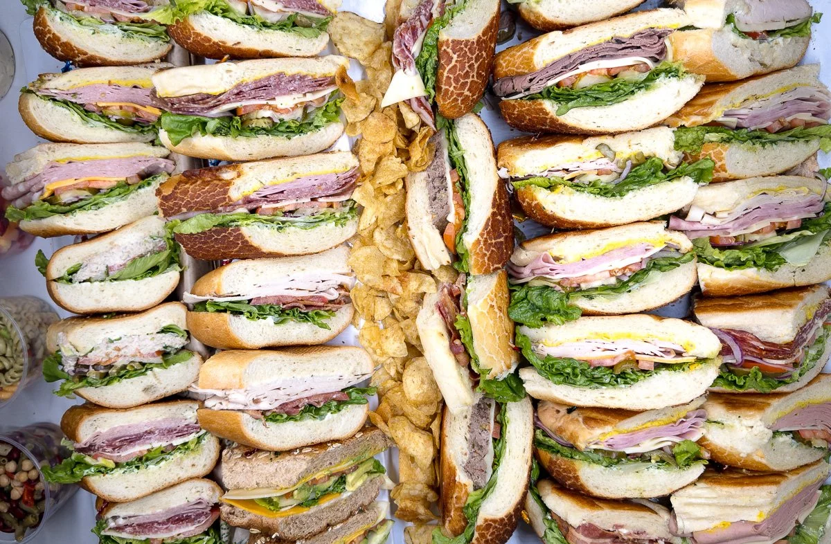 Several sliced sandwiches with various meats, lettuce, and cheese arranged on a table, along with potato chips in the center.
