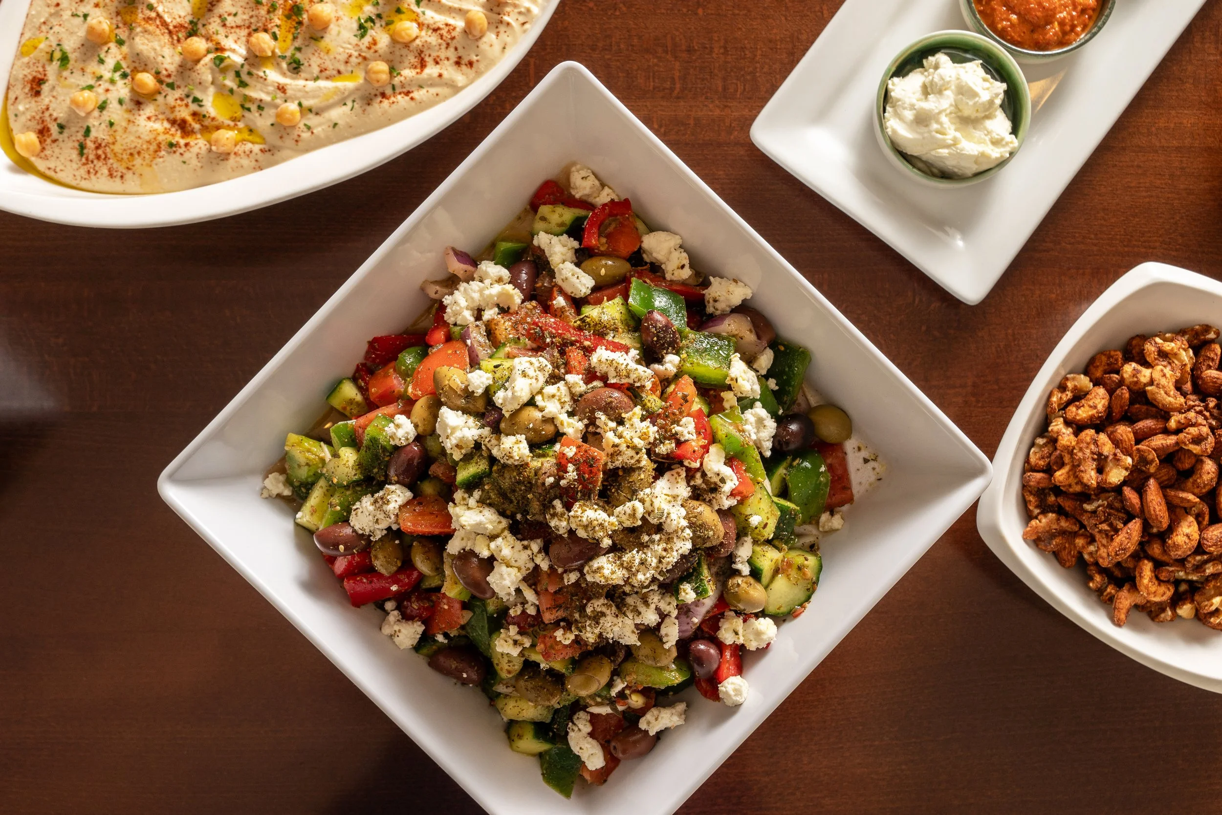 Assorted Mexican dishes on a wooden table, including a bean dip, a fresh vegetable salad with feta cheese, and various salsas.