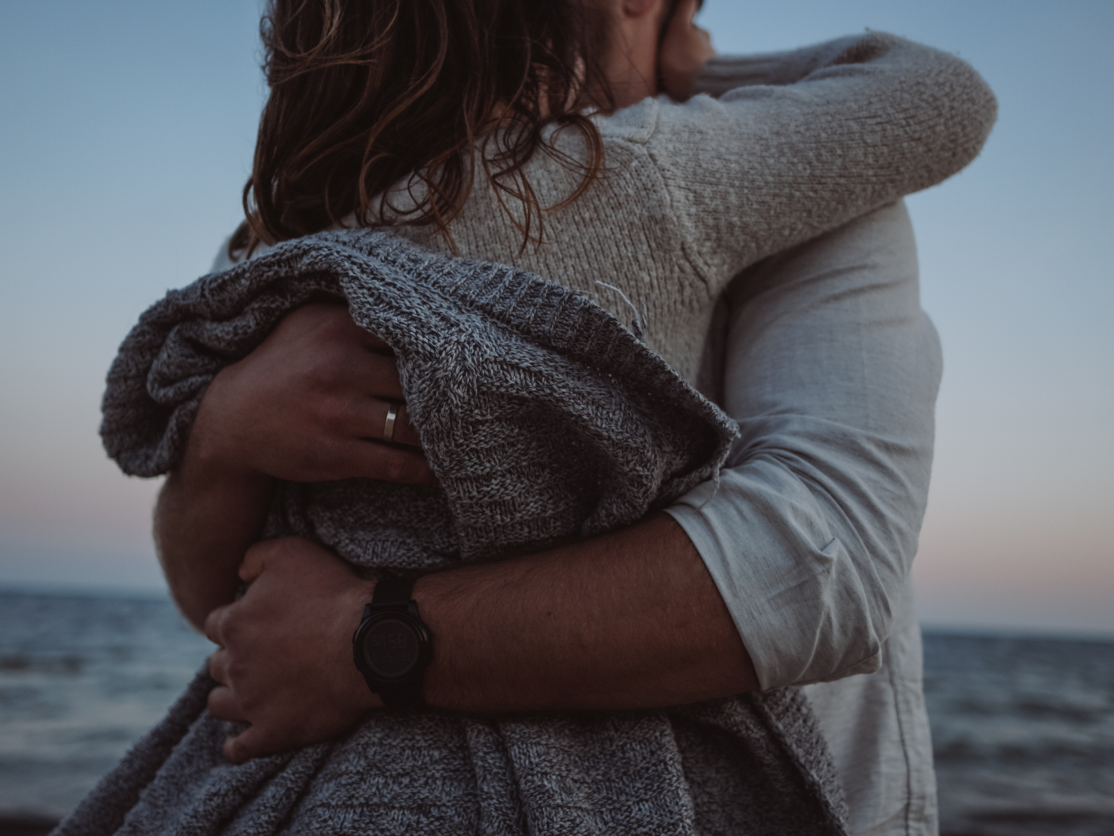A person holding a baby wrapped in a blanket near the ocean at sunset.