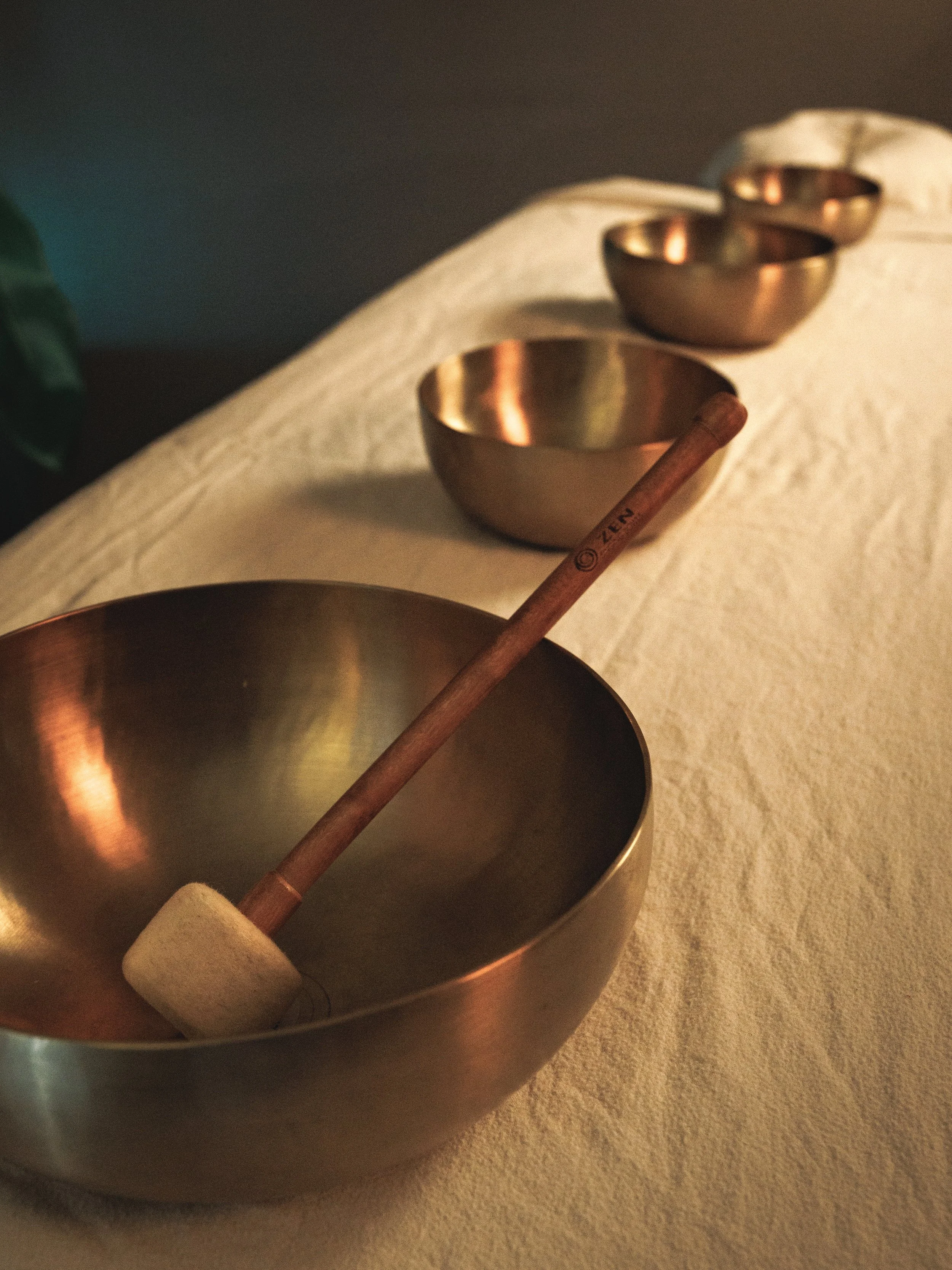 Therapeutic singing bowls on a sofly lit massage table.  A peaceful atmosphere for vibrational sound therapy, relaxation, meditation and deep rest.