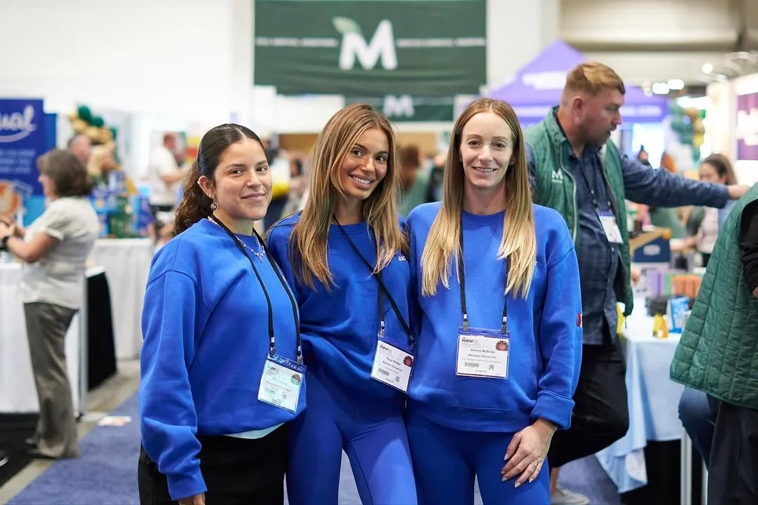 Three women standing together and smiling.