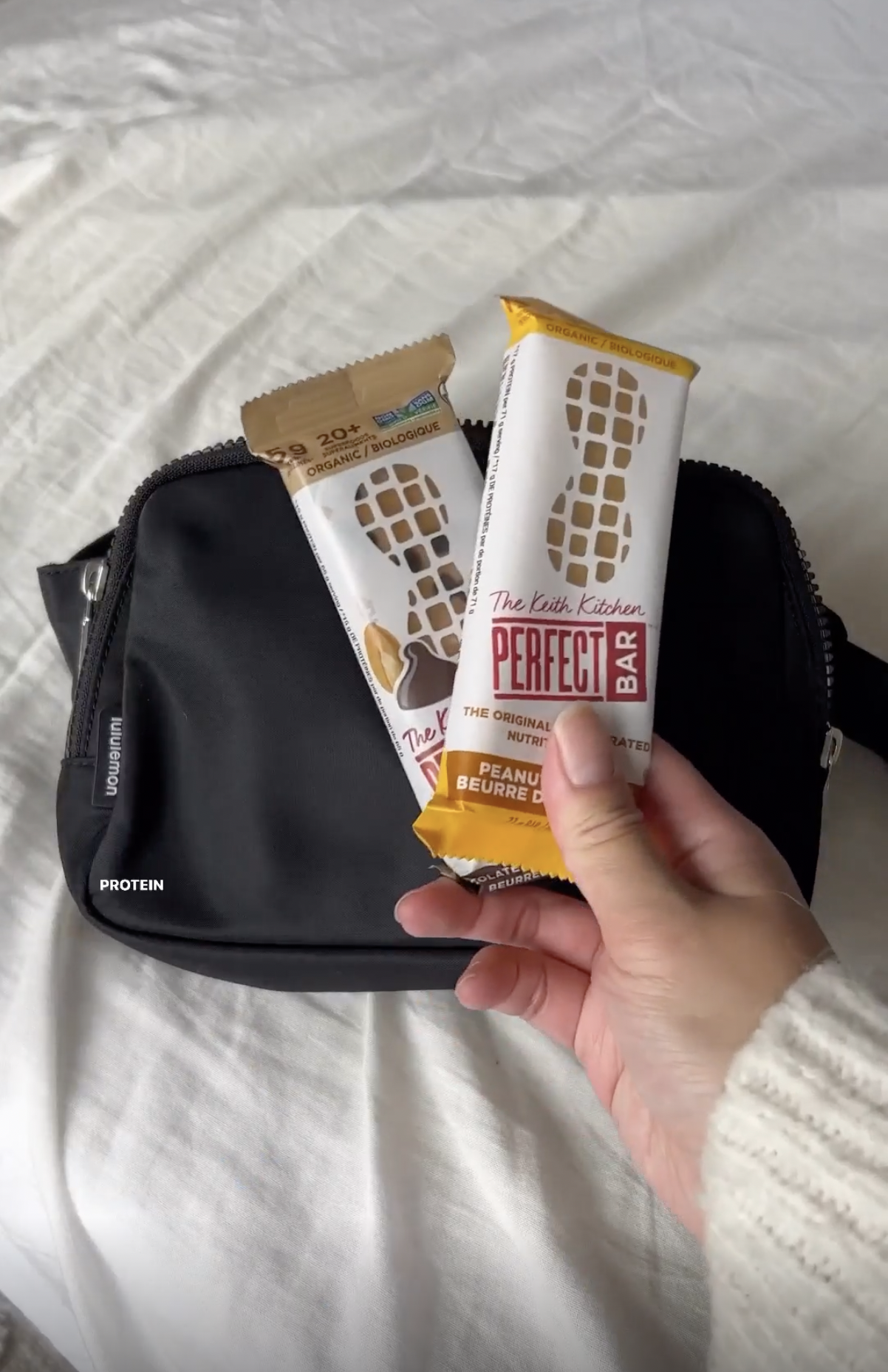 A hand holding two Perfect Bar protein bars.