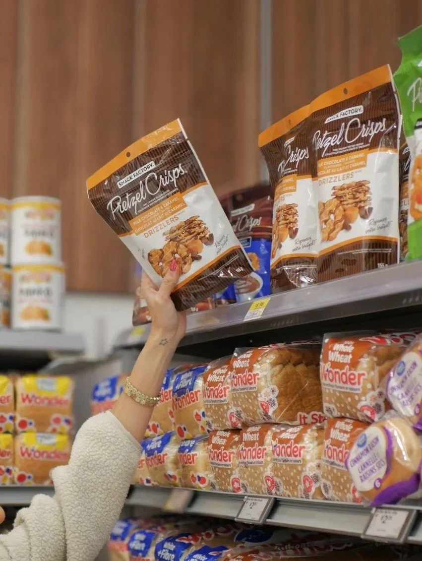 Arm grabbing a bag of pretzel chips off of a grocery store shelf.