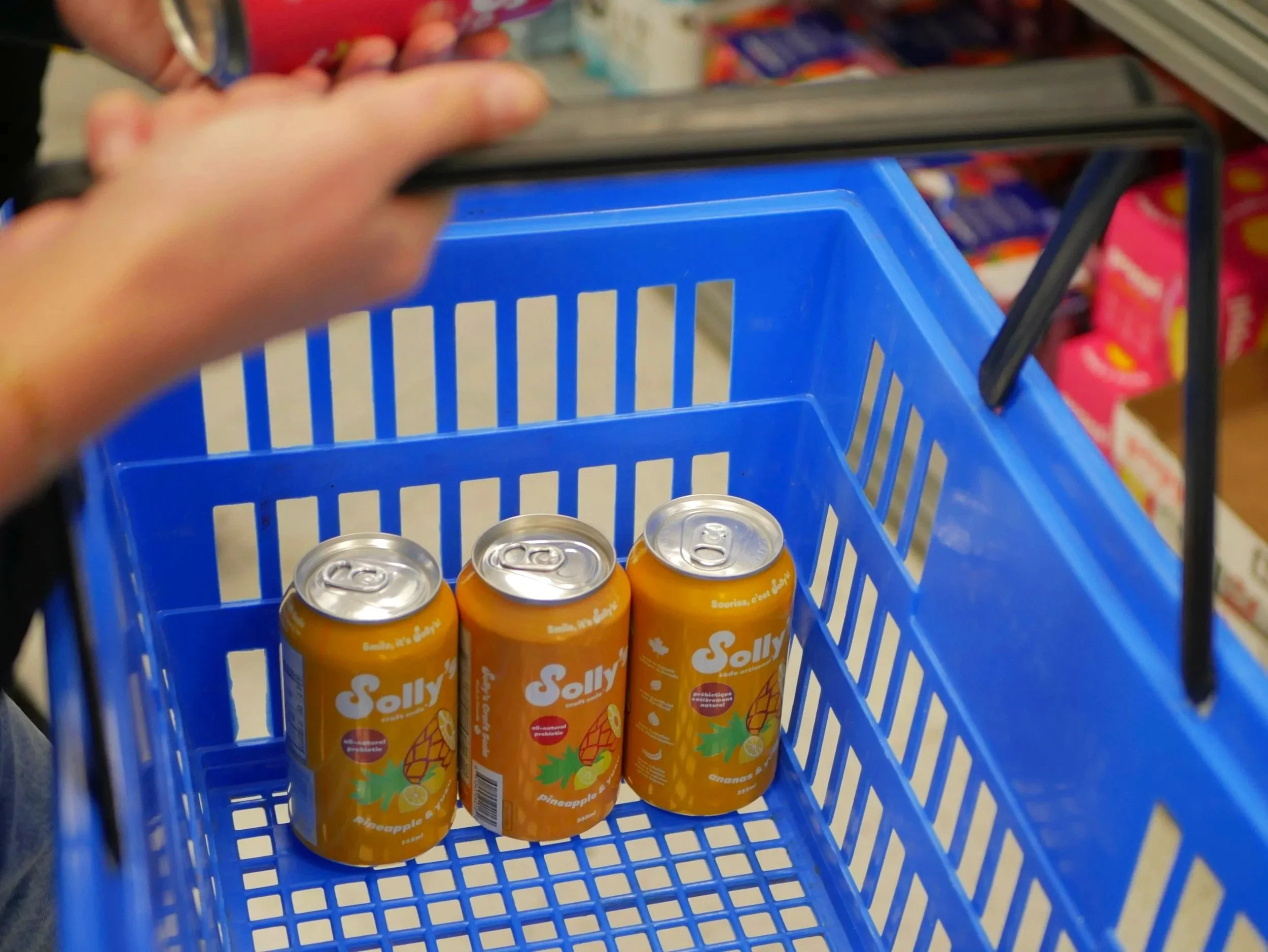 Three cans of soda in a grocery store basket.