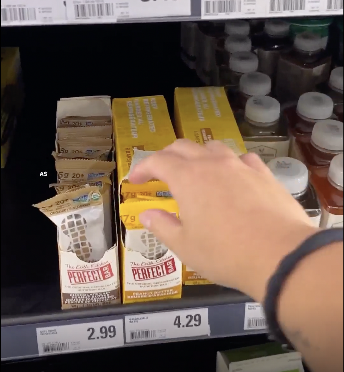 A hand grabbing for a Perfect Bar protein bar on a grocery store shelf.