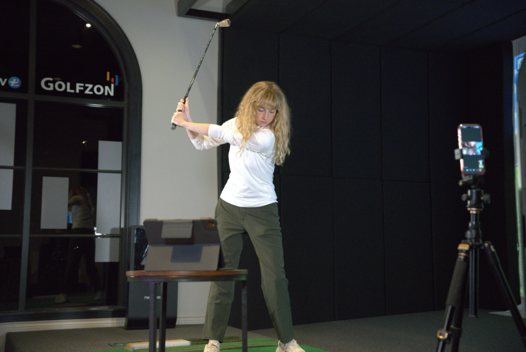 Woman practicing golf swings in indoor simulator room at land run links