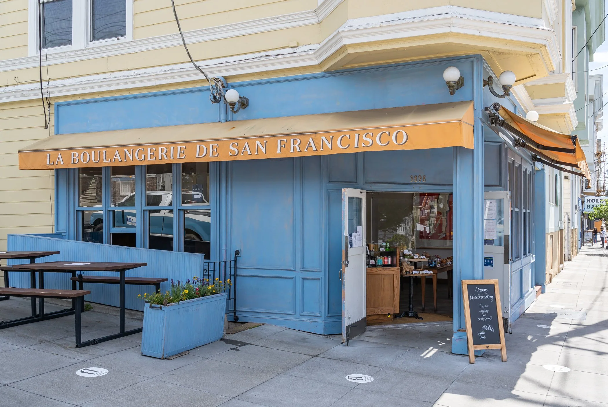 Exterior of a corner café named 'La Boulangerie de San Francisco' with a blue storefront, orange awning, and outdoor seating area.