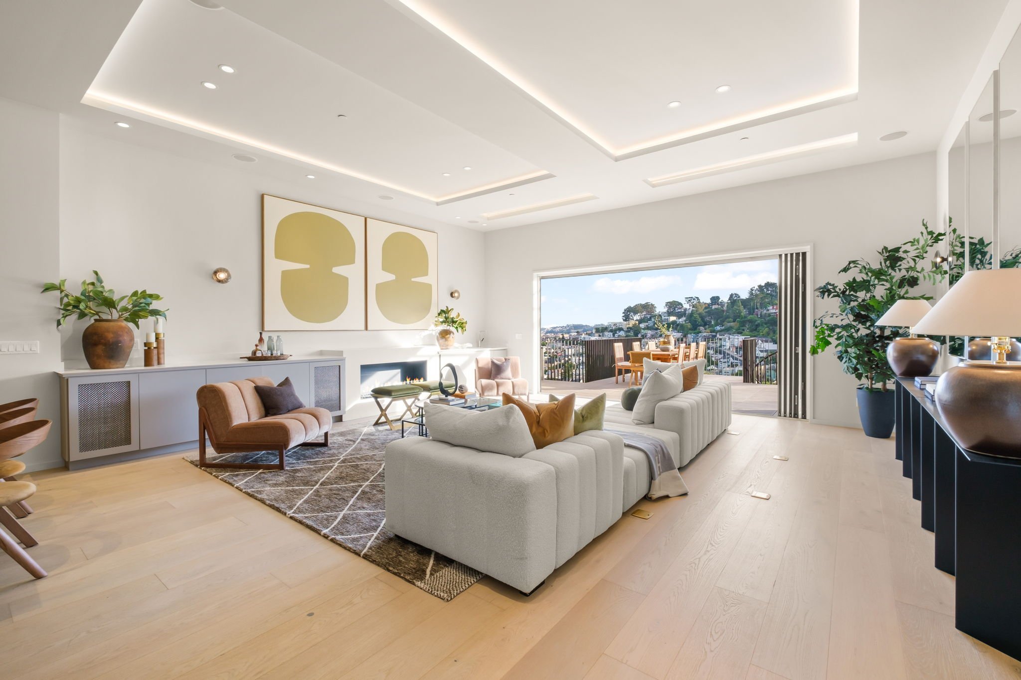 Bright living room with white walls, modern art, colorful cushions, and large sliding doors opening onto a balcony with outdoor dining.