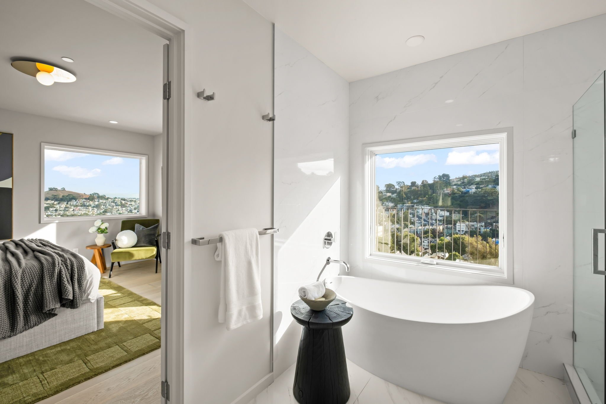 Modern bathroom with a free-standing bathtub, large window with a city view, and a walk-in shower with a glass door.
