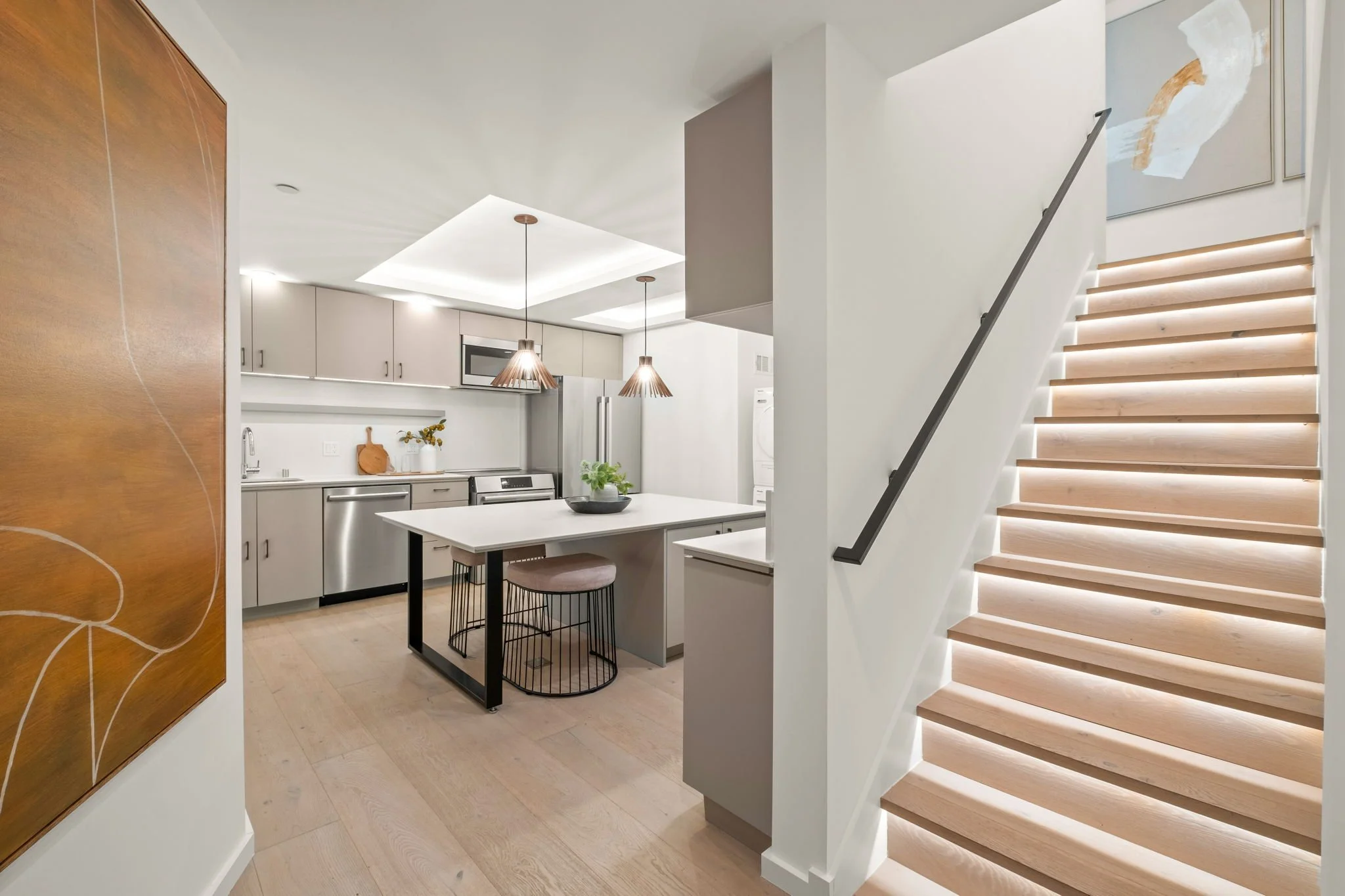 Modern kitchen and staircase with wooden steps and black handrail.
