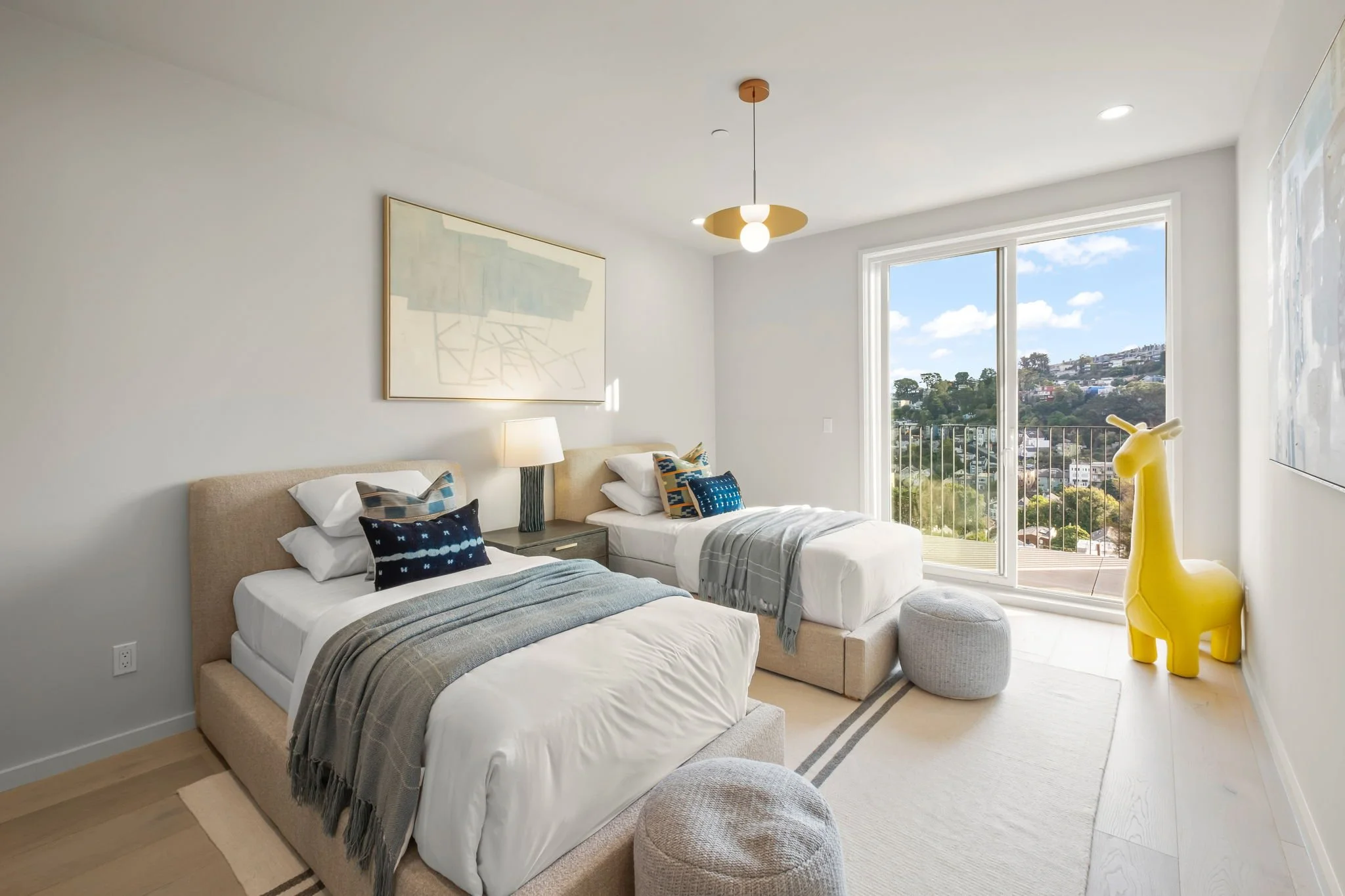 A modern bedroom with two twin beds, a nightstand, a lamp, large window with a view, and yellow giraffe sculpture.