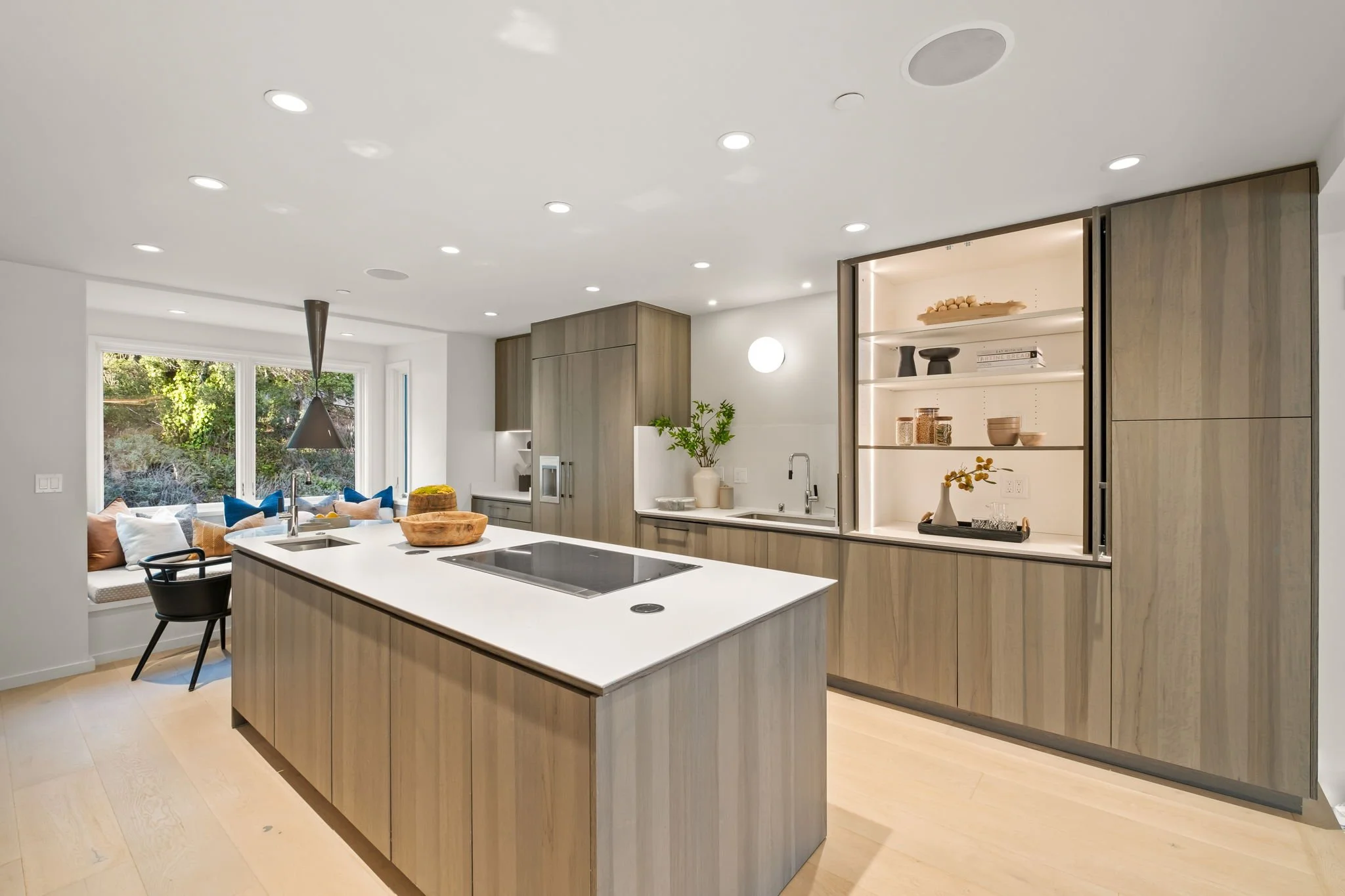 Modern open-concept kitchen with a large island, built-in shelving illuminated with LED lights, and a cozy window seat with pillows.