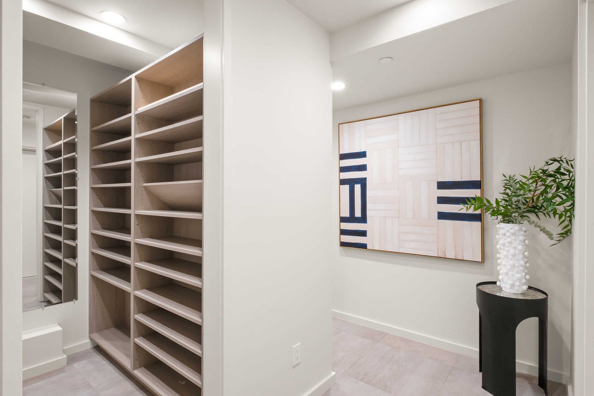 Interior of a modern home with built-in wooden shelves, a large abstract wall art, and a decorative white vase with green plants on a black pedestal