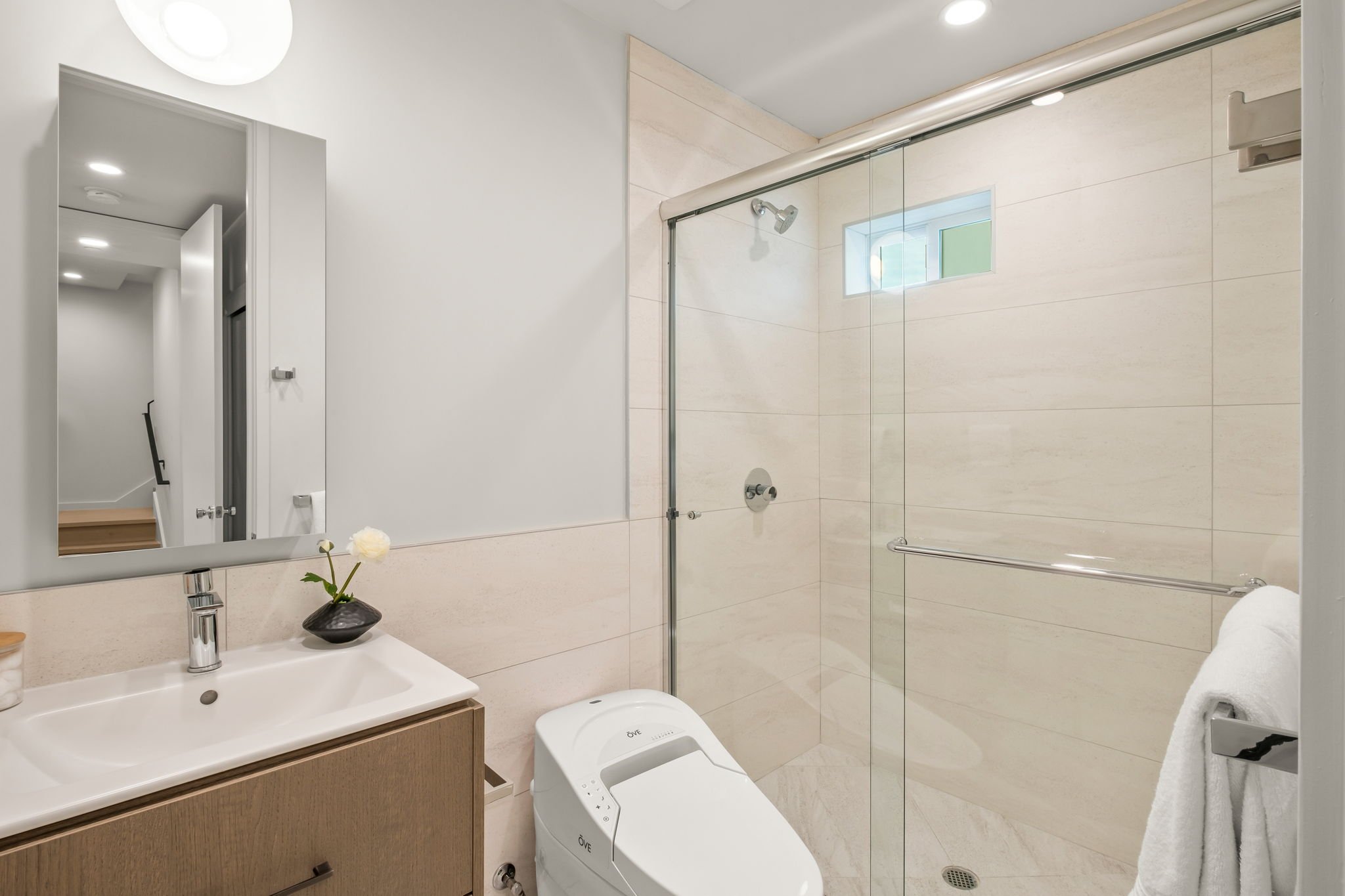Modern bathroom with a walk-in shower, vanity with a mirror and sink, toilet, and a towel hanging on a rack.