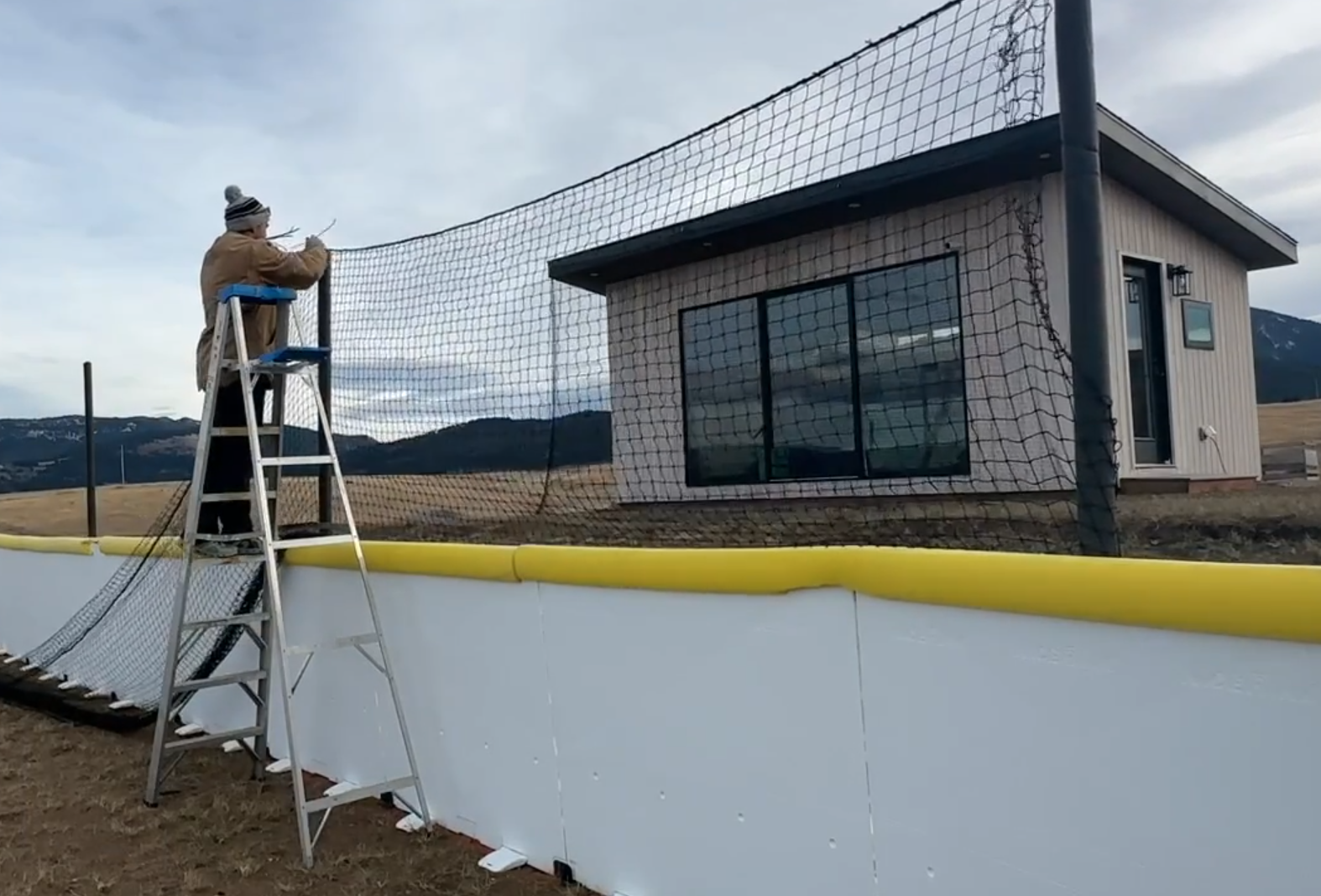 On ladder, putting up netting around backstop of hockey rink