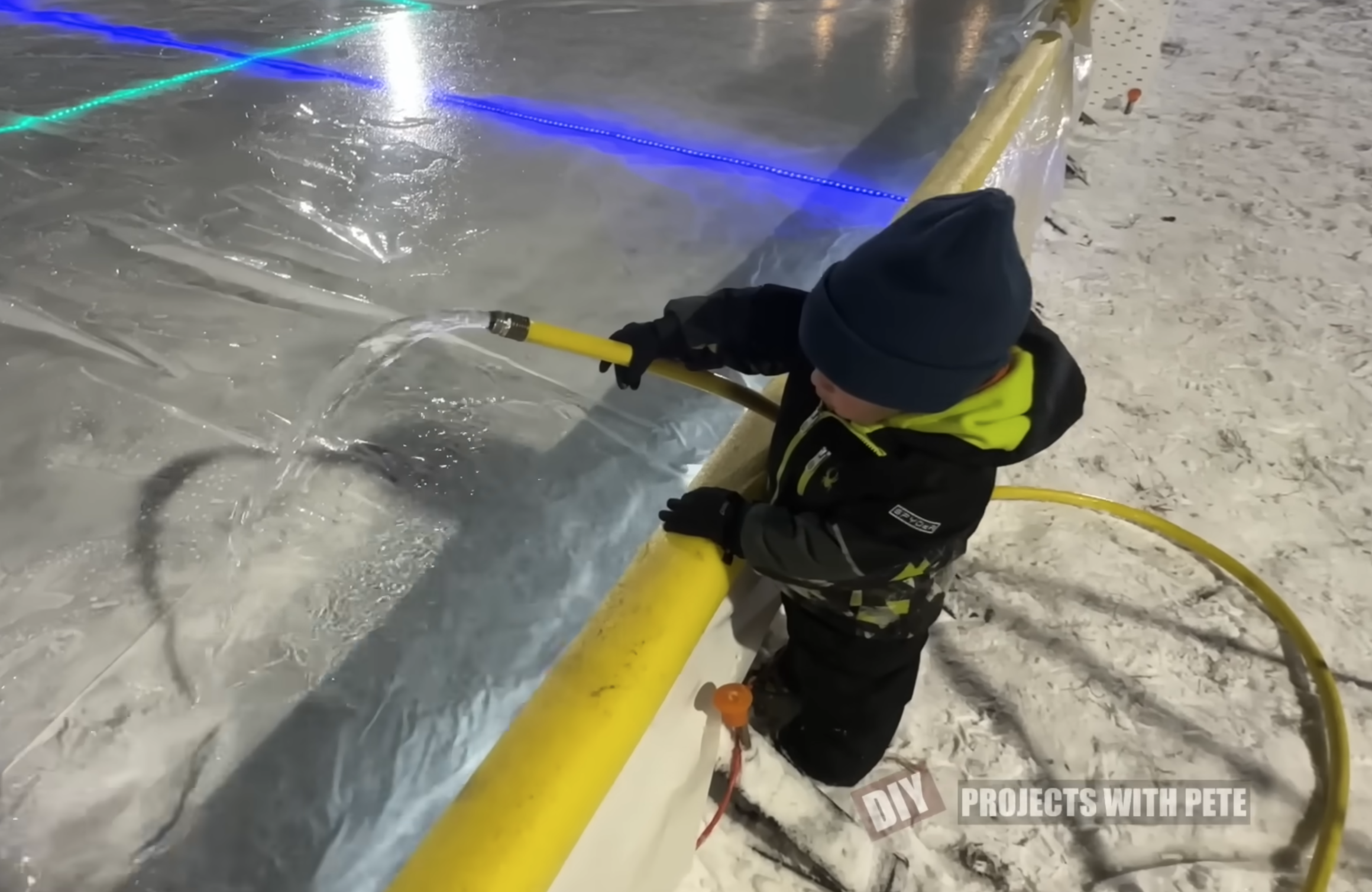 young child helping fill the ice rink with garden hose