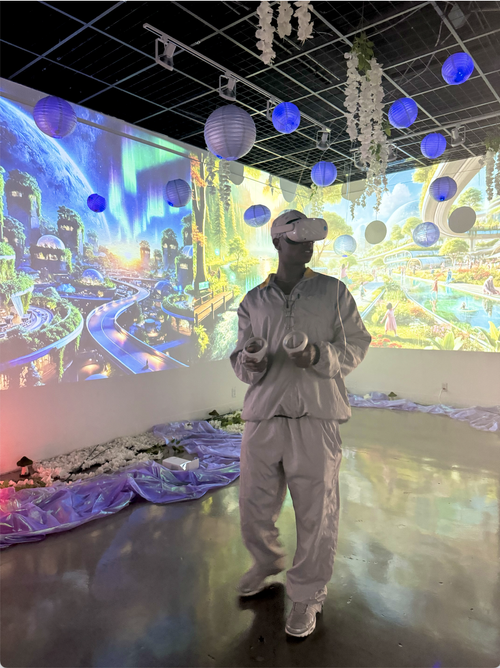 Person wearing a virtual reality headset and holding controllers in a room with vibrant digital projection of a futuristic cityscape, blue and white hanging lanterns, and decorative flowers.