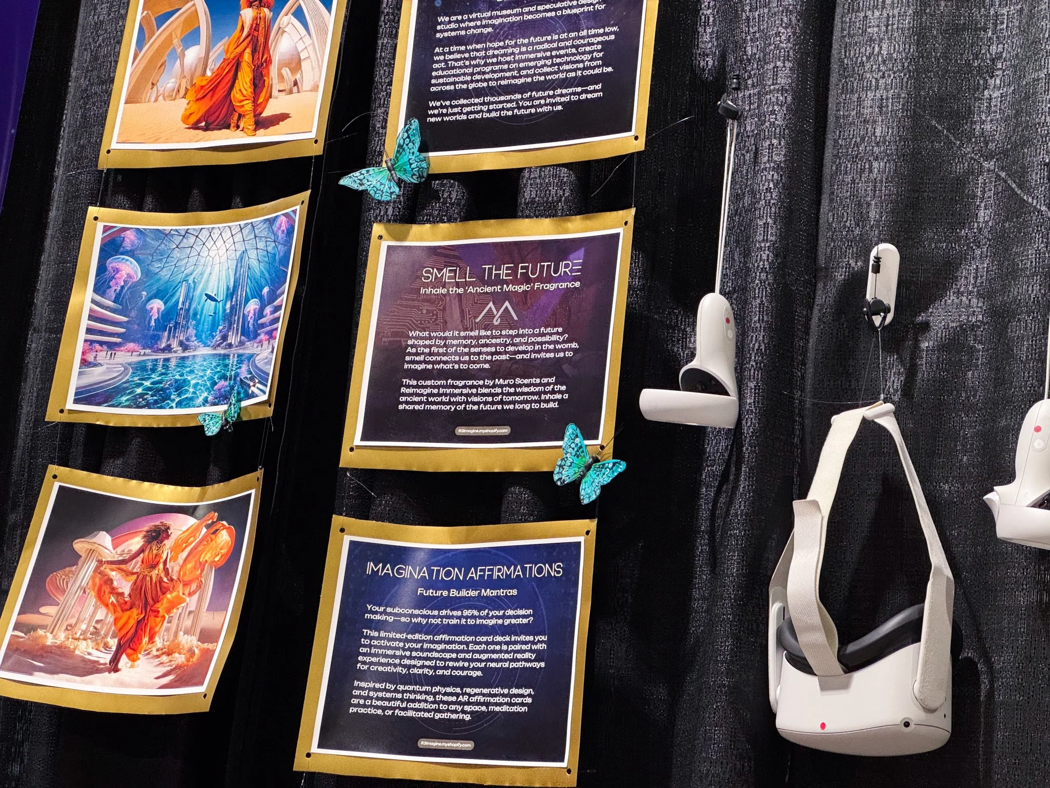 A display wall featuring several colorful posters and decorations about imagining the future, with images of fantasy landscapes, futuristic architecture, and a figure in flowing orange clothing. Blue butterflies are attached to some of the posters. There are two white virtual reality headsets hanging on the right side of the display.