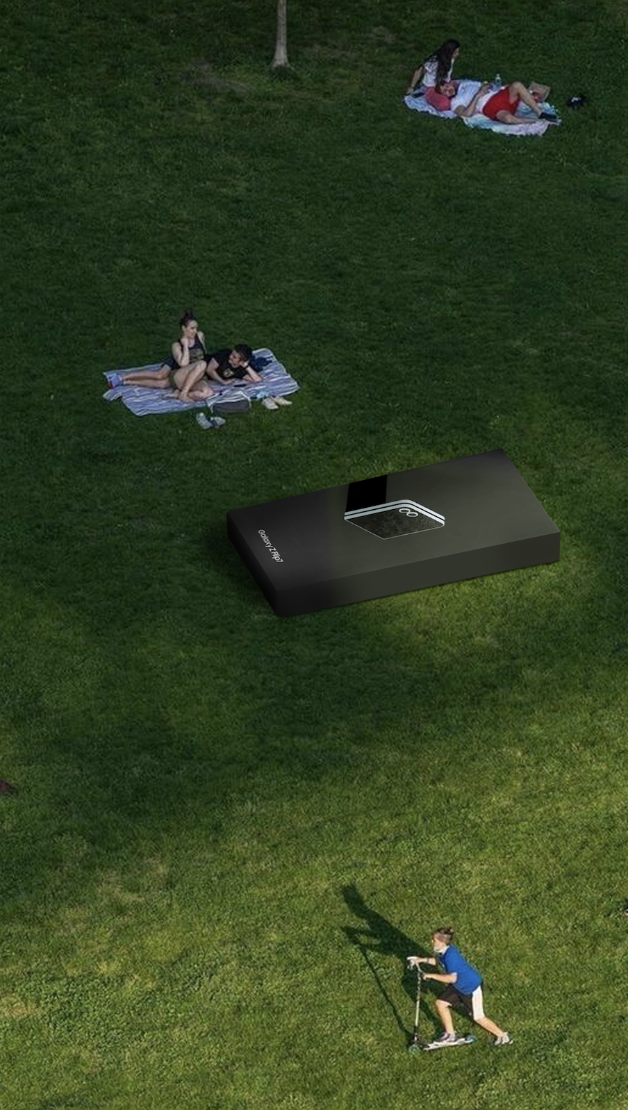 A group of people are on a grassy field with a Galaxy Flip 4 smartphone blocking the view, creating a visual illusion of a giant phone. Two people are lying on a blanket at the top, two are sitting on a blanket in the middle, and a child is riding a scooter at the bottom, with a sun shadow cast on the grass.