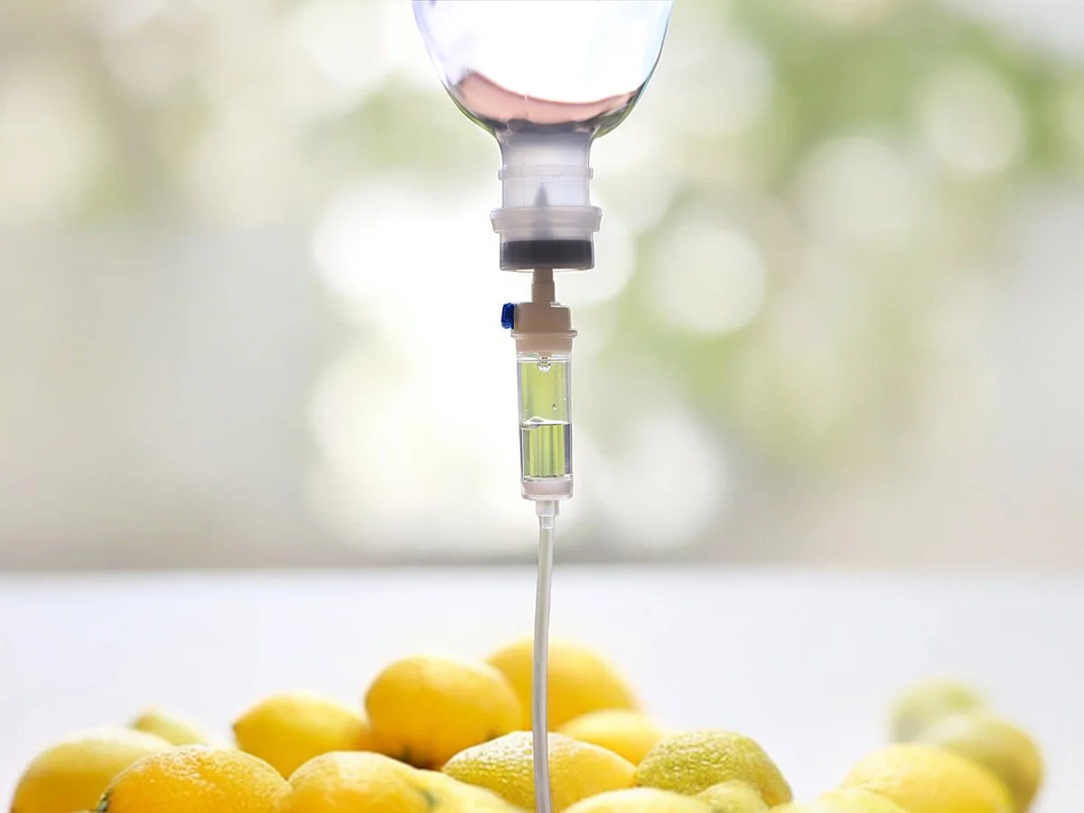 Close-up of an IV drip bag hanging above a pile of yellow lemons with a blurred background.