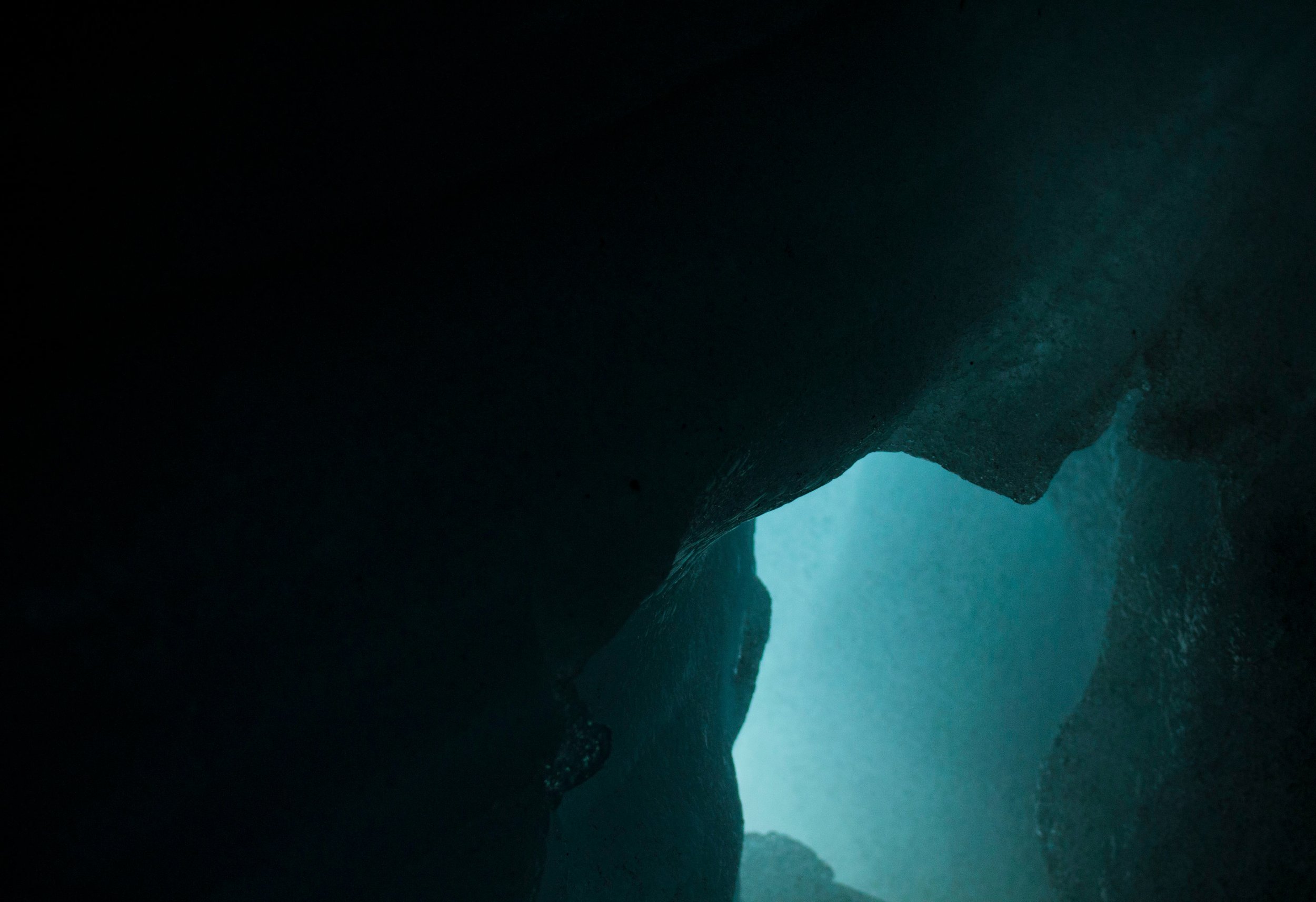 Vue à travers un trou dans une roche sombre vers une lumière bleue dans une grotte ou un canyon.