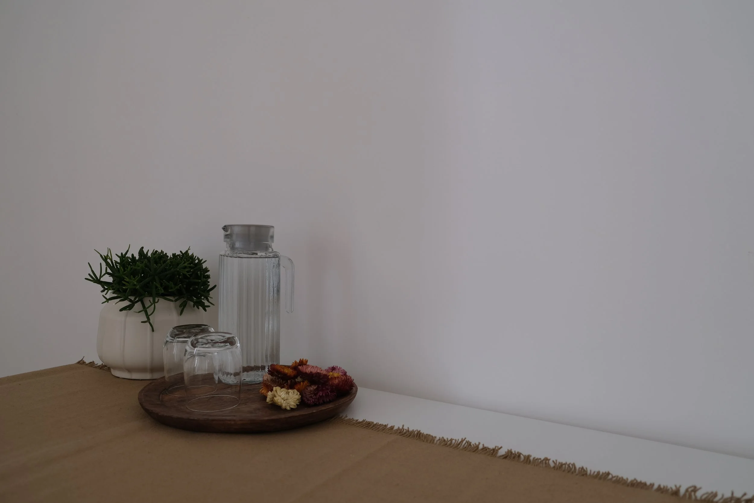 Décoration minimaliste avec une plante en pot blanc, un vase en verre, des verres, et un plateau en bois avec des fleurs séchées sur une table en bois, contre un mur blanc.
Chambre Airbnb calme à Lecce dans les pouilles