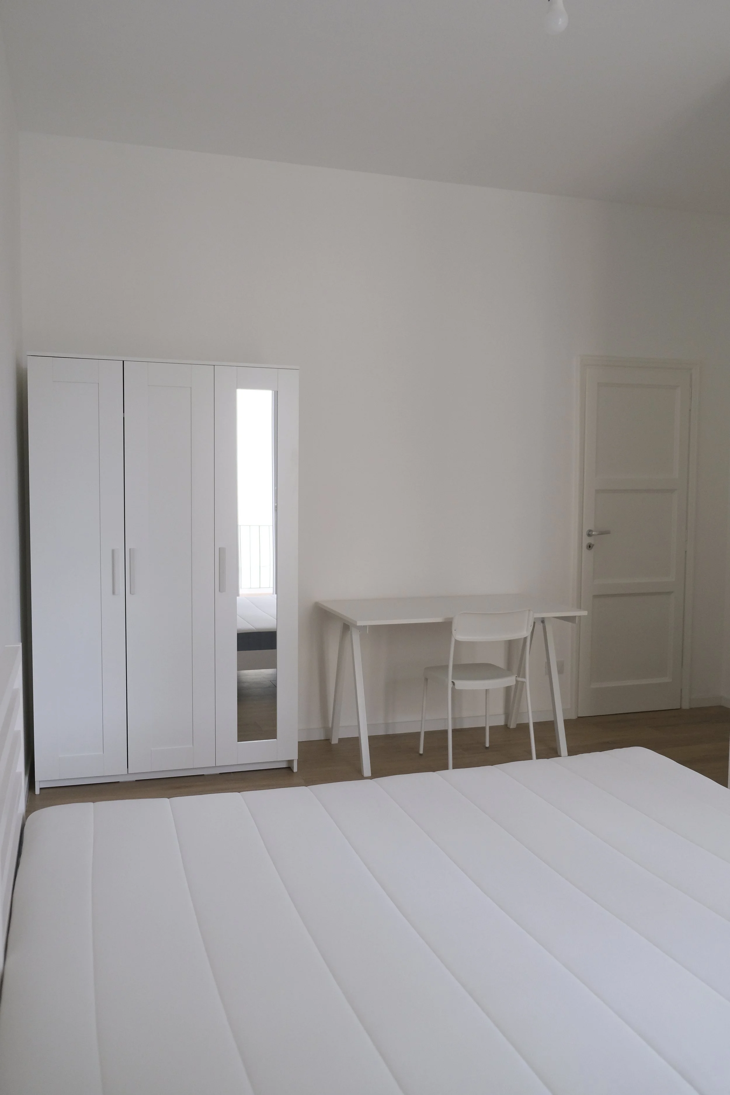 Chambre blanche avec lit, armoire, bureau et chaise.