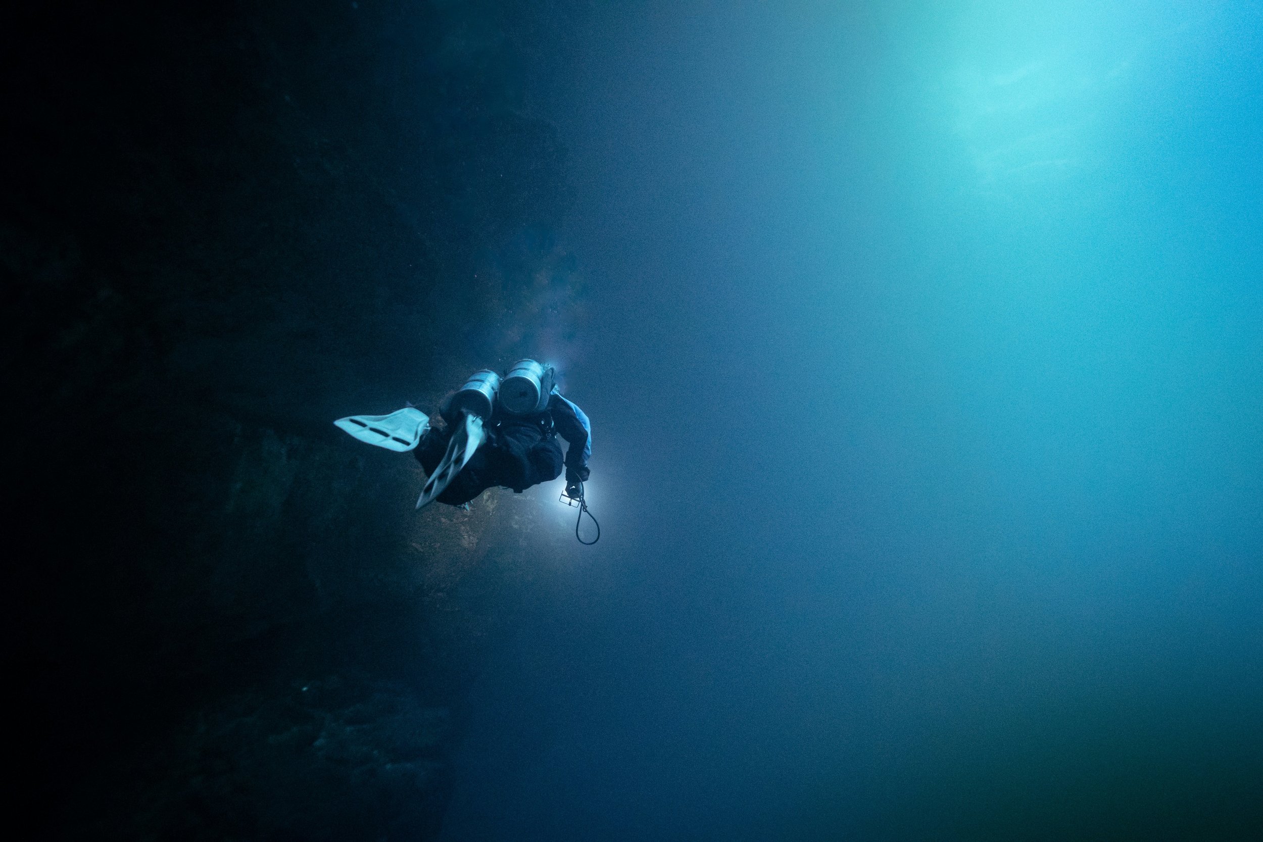 Plongée sous-marine dans une grotte, plongeur avec équipement de plongée en apnée, éclairage naturel filtrant à travers l'eau.