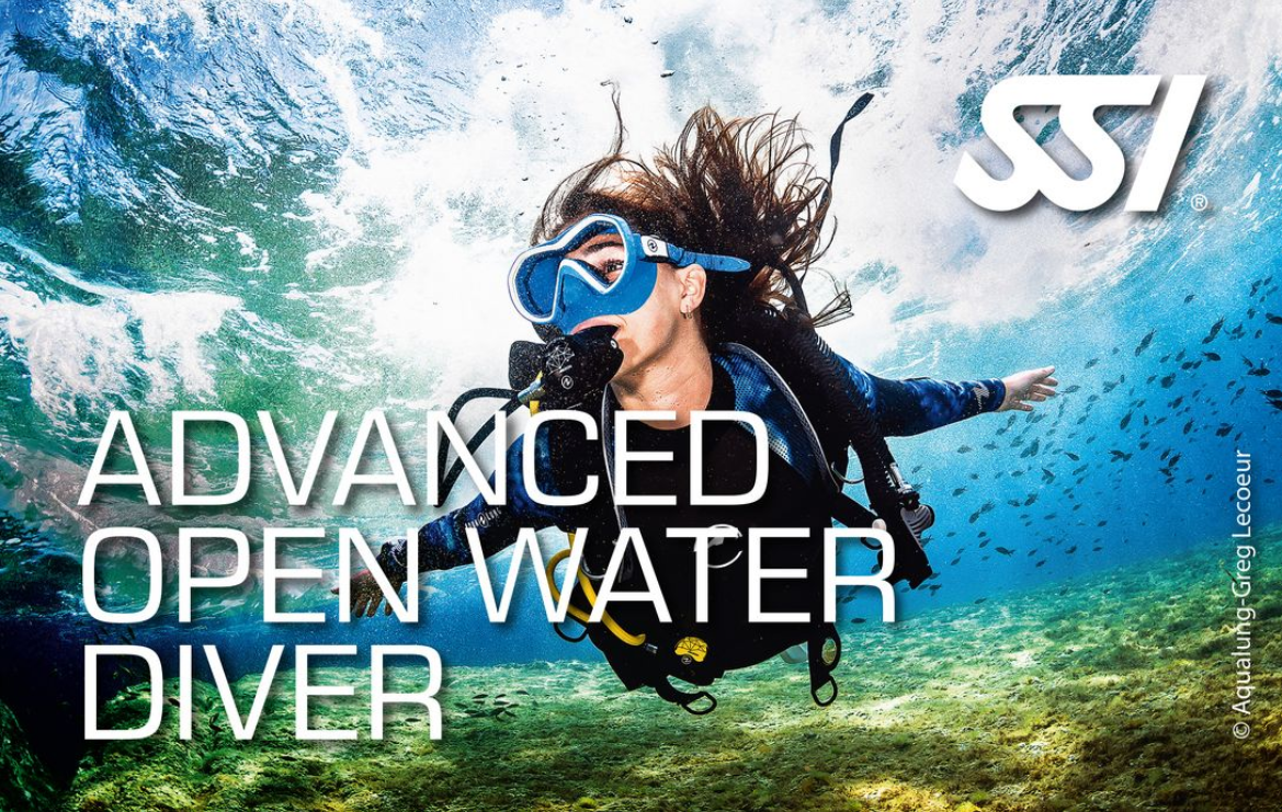 Une femme pratiquant la plongée sous-marine en eau libre avec un équipement complet, et un gilet de flottabilité, nageant sous la surface de l'eau avec des poissons autour, dans un environnement marin coloré. Formation SSI Advanced open water diver