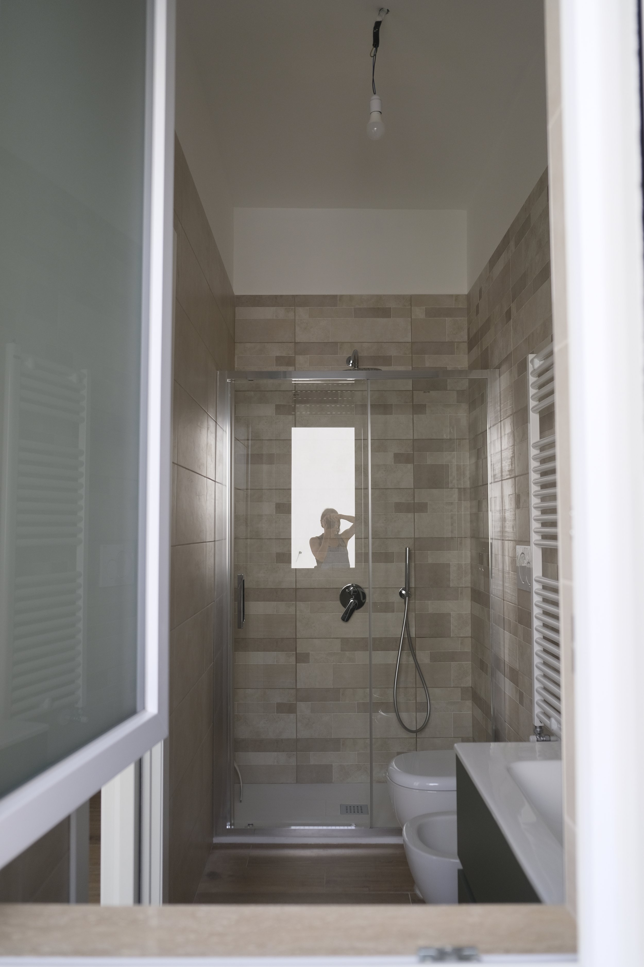 Vue du miroir d'une salle de bain moderne avec douche en verre, toilettes, lavabo blanc et radiateur blanc, vue depuis une fenêtre ouverte.