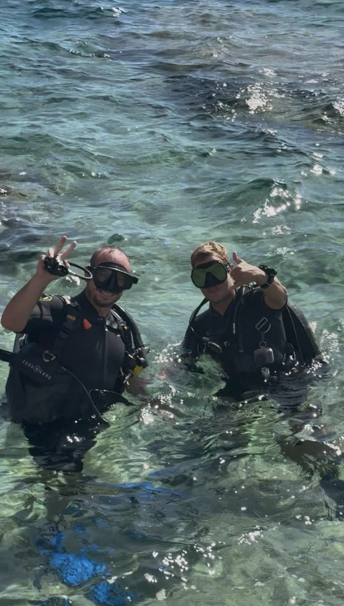 Deux plongeurs portant des équipements de plongée en mer, faisant un signe de paix et un pouce levé, avec un fond d'eau claire et calme. Instructeur de plongée privé, sud de l'italie dans les pouilles