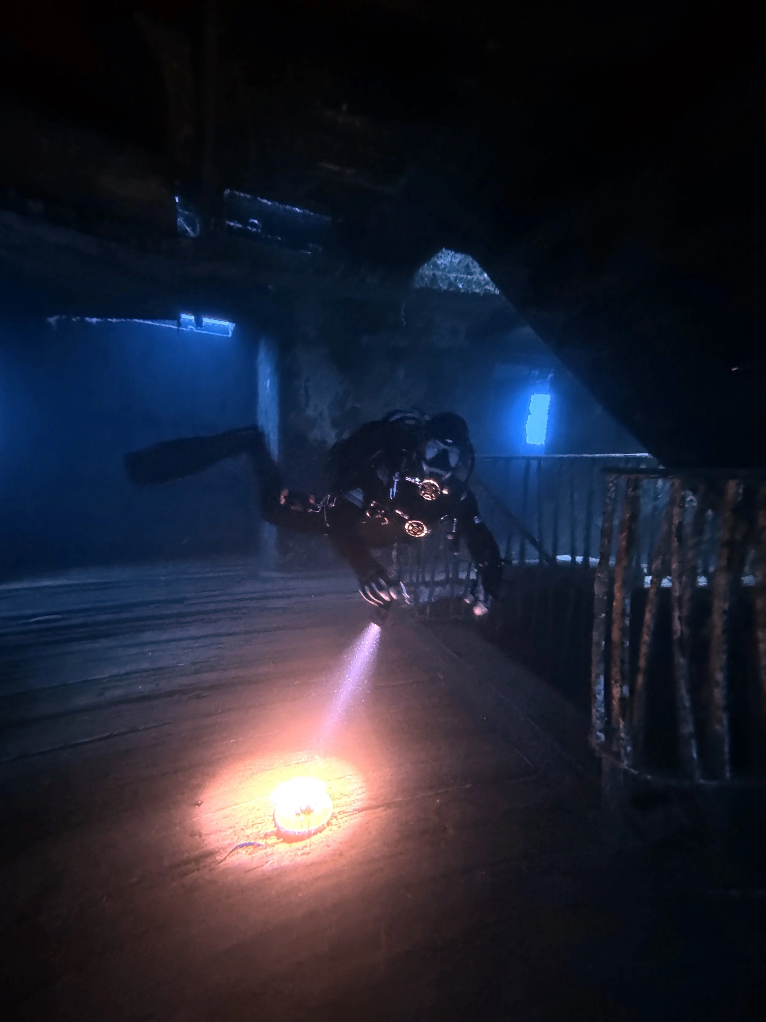 Plongée sous-marine dans une caverne ou un bâtiment abandonné, avec un plongeur utilisant une lampe torche pour explorer l'endroit sombre.