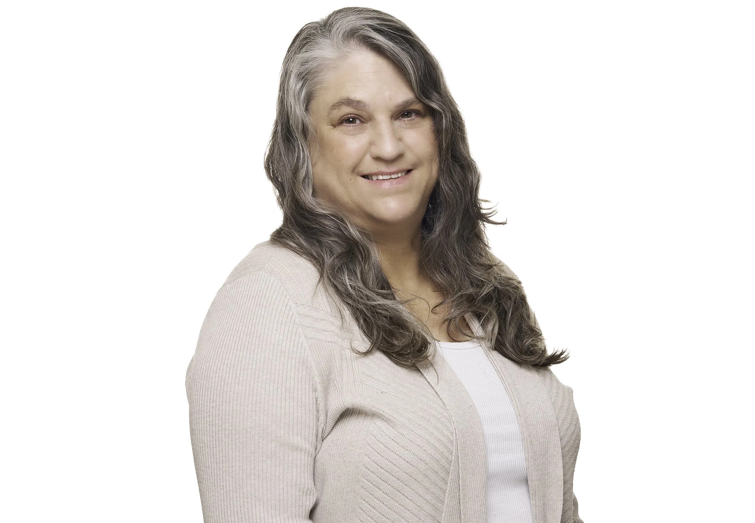 A woman with long gray hair, smiling, wearing a beige cardigan over a white top, facing slightly to the right against a plain white background.