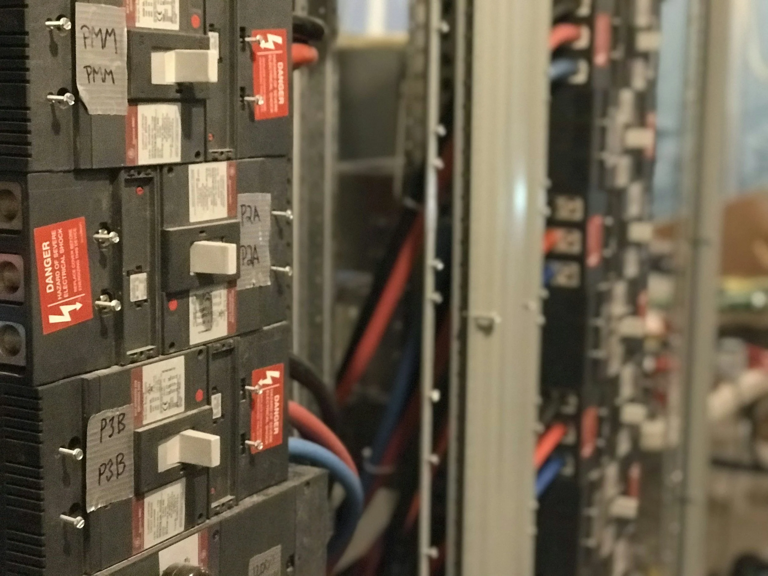 Close-up of electrical circuit breakers in an electrical panel, with red warning labels and colored wires.