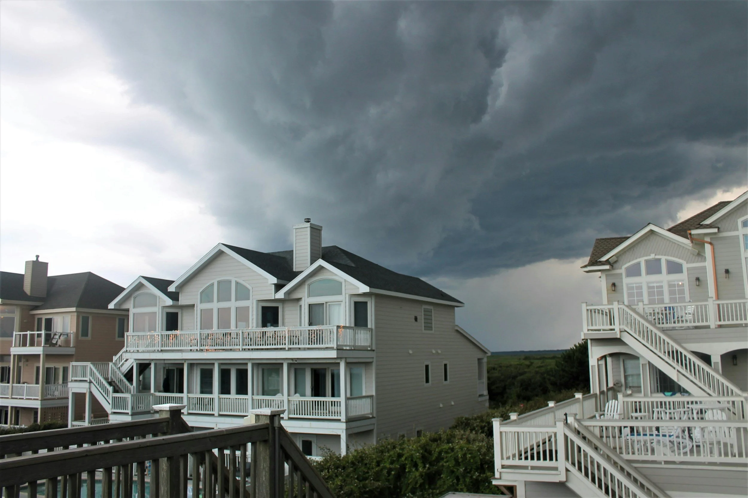 Dark storm clouds over beachfront houses with decks and stairs.