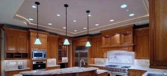 A spacious kitchen with wooden cabinets, granite countertops, a stainless steel refrigerator, oven, microwave, and a sink under a window. Pendant lights hang from the ceiling.