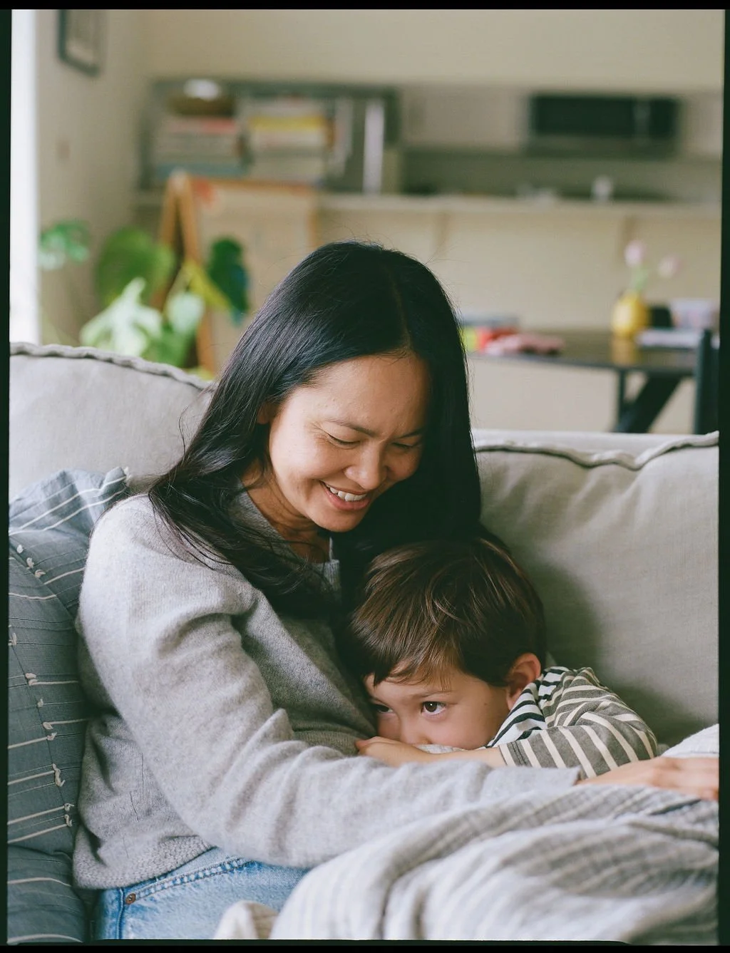 A woman and a young boy sitting together on a couch, smiling and cuddling.
