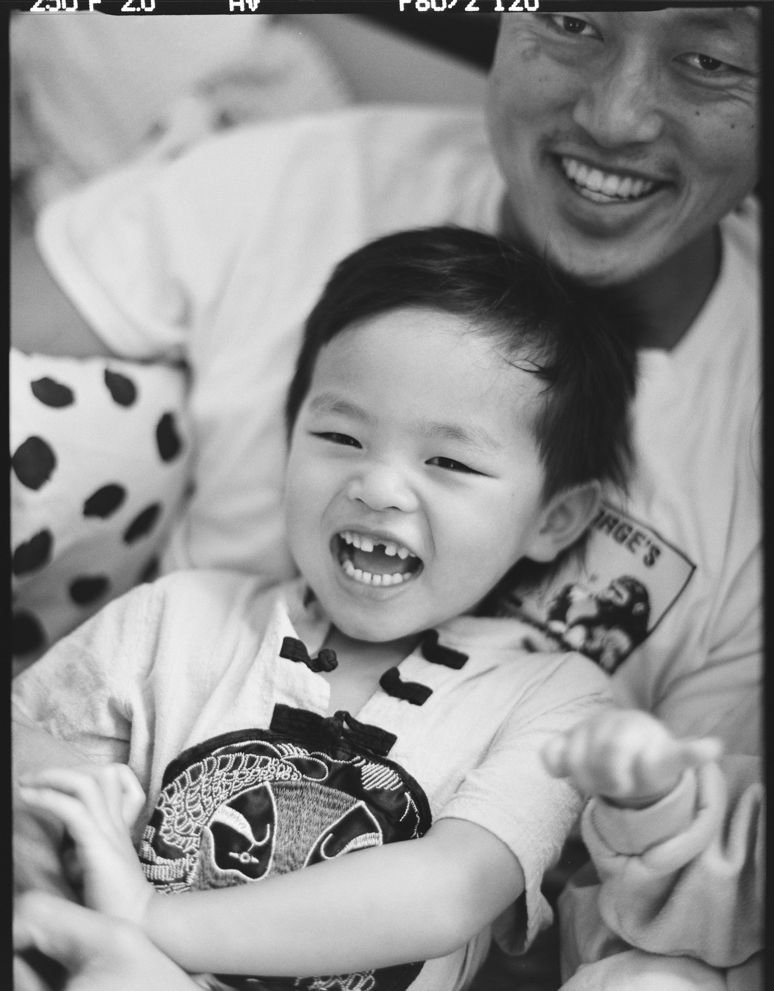 black and white medium format photo of a father and his 3 year old son smiling and laughing at the camera, this photo was taken in their home in San Francisco, California. 