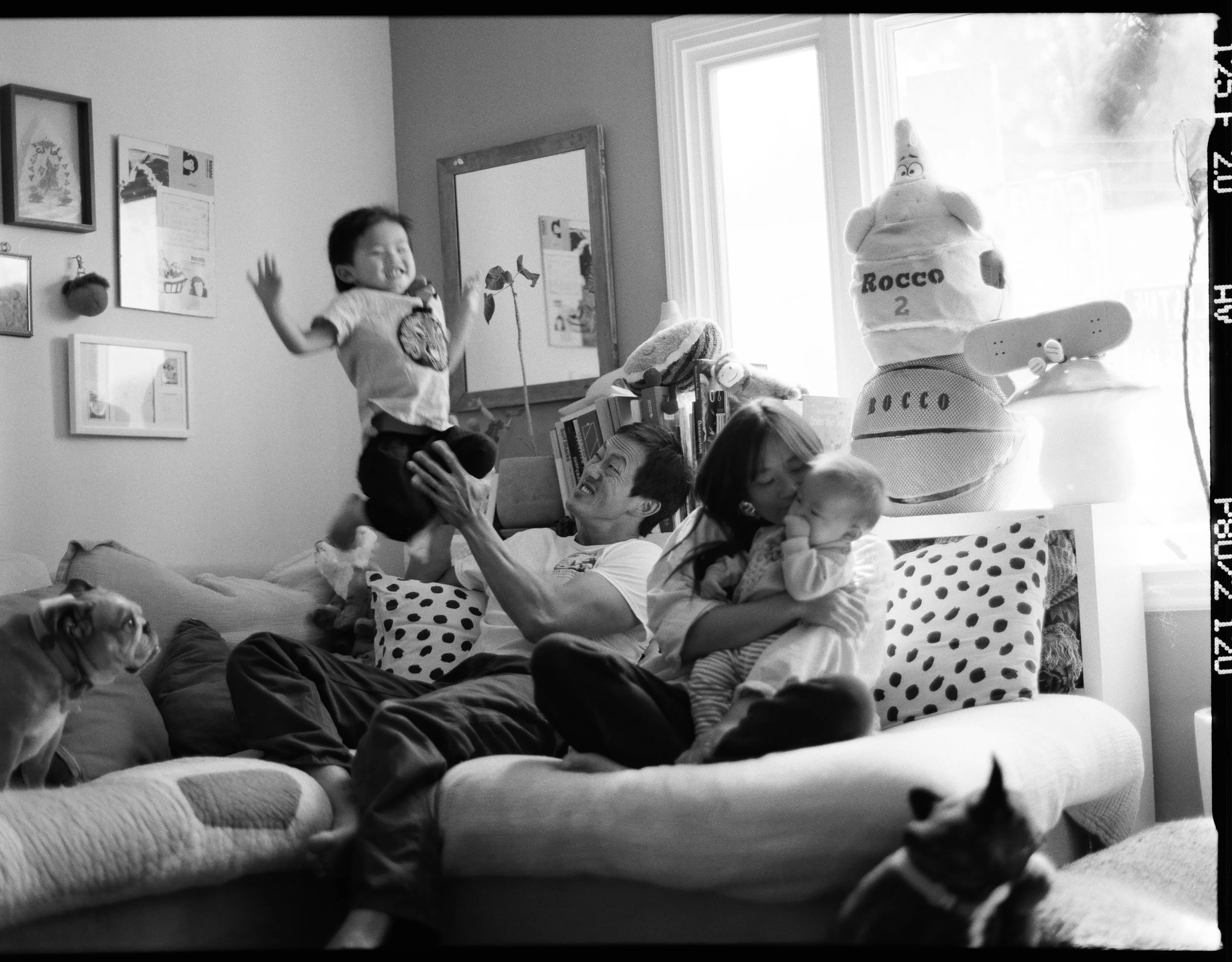 black and white medium format family photo of an asian family, a mother, father, an infant and a toddler sitting and laughing on their couch in their home in San Francisco, California. 